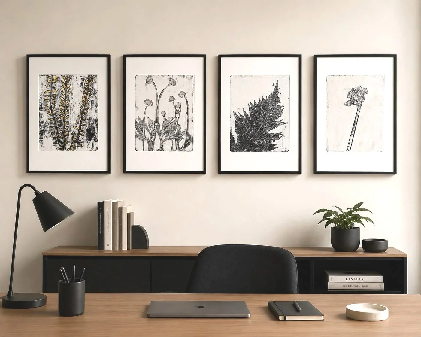 Modern workspace with four black-framed botanical artwork prints on the wall, a wooden desk with a closed laptop, notebook, pen, and decorative tray, black desk drawer with books and a small plant, black desk lamp, black pen holder, and a shelf with books and potted plants.