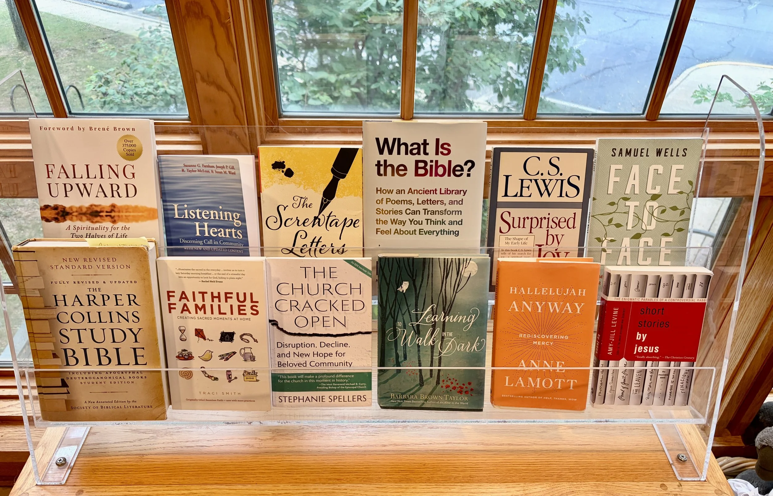 Episcopal Church of the Holy Cross: A dozen books on display in front of a window. Books include the Bible, and works by C.S. Lewis, Richard Rohr, Anne Lamott, Barbara Brown Taylor, Sam Wells, and Stephanie Spellers.