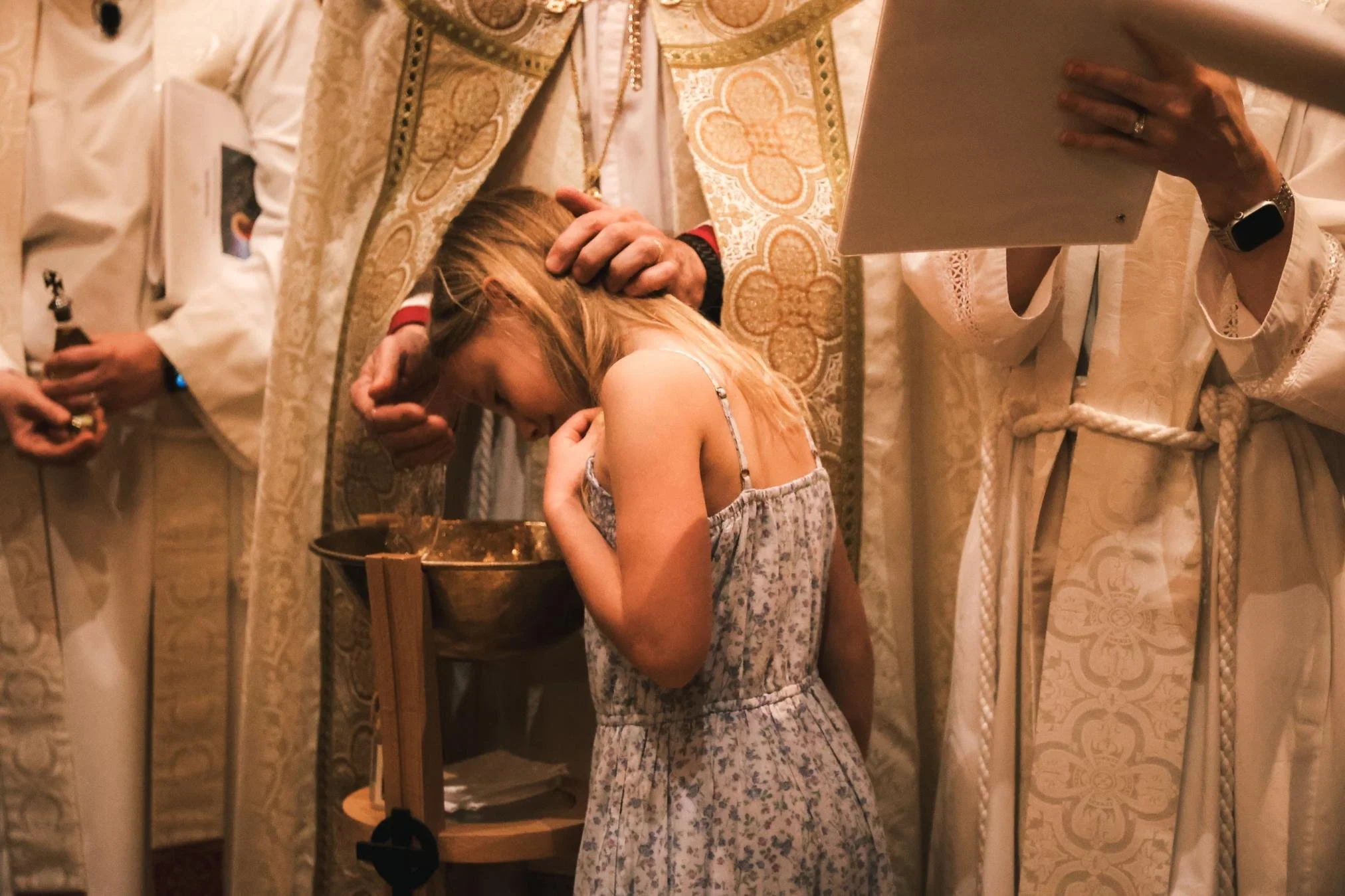 Holy Cross Episcopal Church: A religious ceremony with a priest blessing a young girl who is kneeling with her head bowed and eyes closed.
