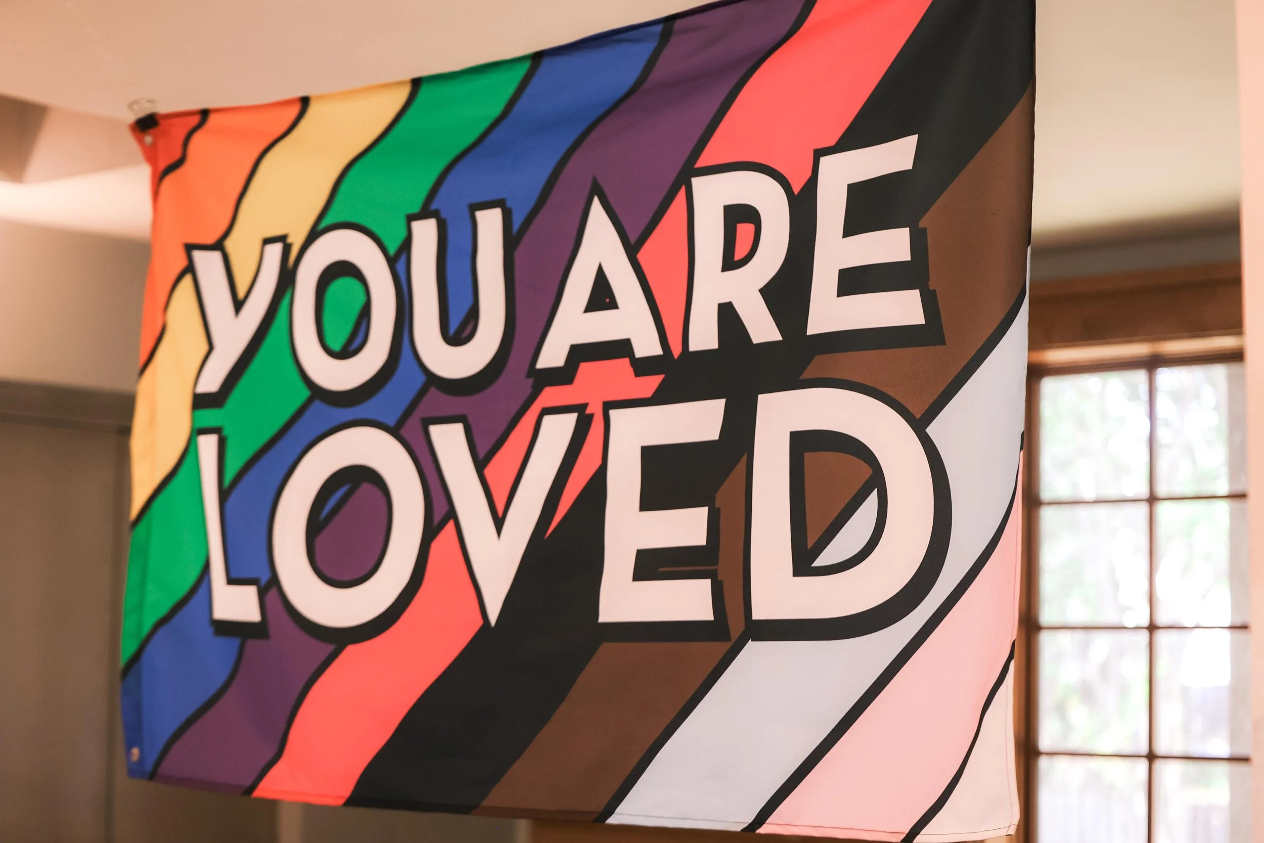 Holy Cross Episcopal Church: Flag with rainbow colors and the phrase "YOU ARE LOVED" written across it.