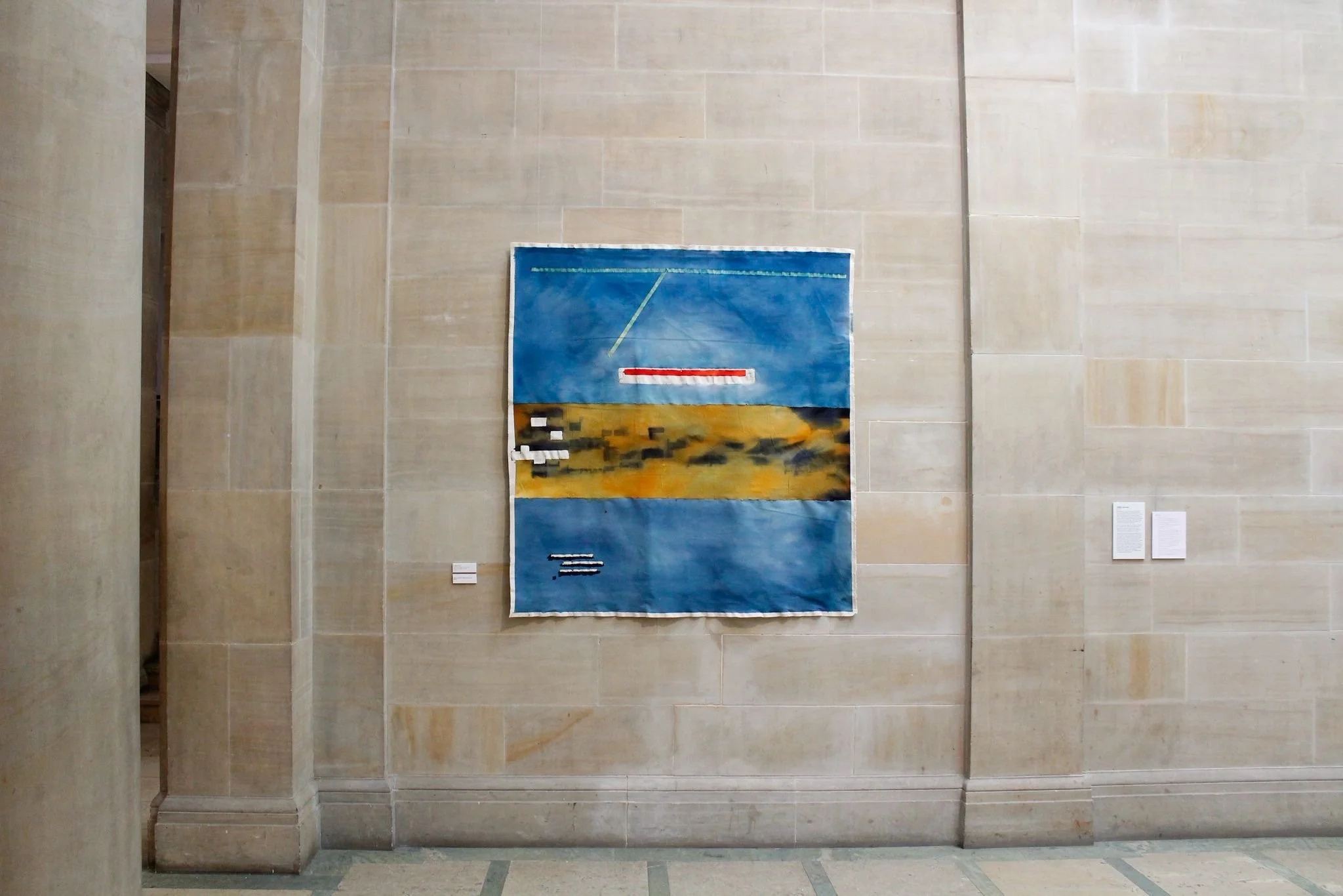 A painting displayed on a beige stone wall in an art gallery, the Royal Scottish Academy. Somewhere Above Ground, original abstract painting by contemporary artist Annabelle Pelaez.