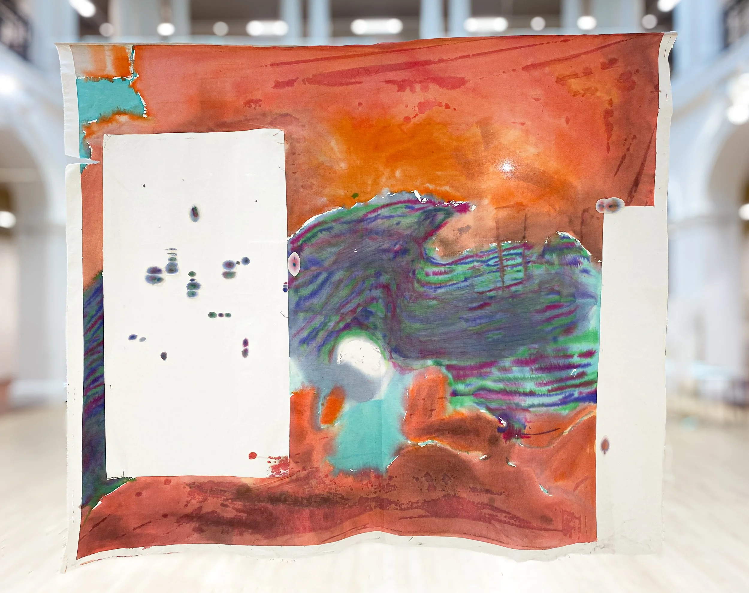 Colorful abstract watercolor painting with red, orange, purple, blue, green, and white hues, displayed on a white surface in a well-lit indoor space.