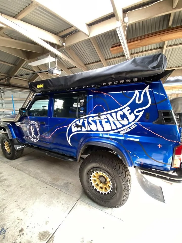 A blue off-road vehicle with large tires parked in a garage. It has a white logo that reads 'Justice' with a flaming torch and the name 'Medra' on the side, and a black canopy on top.