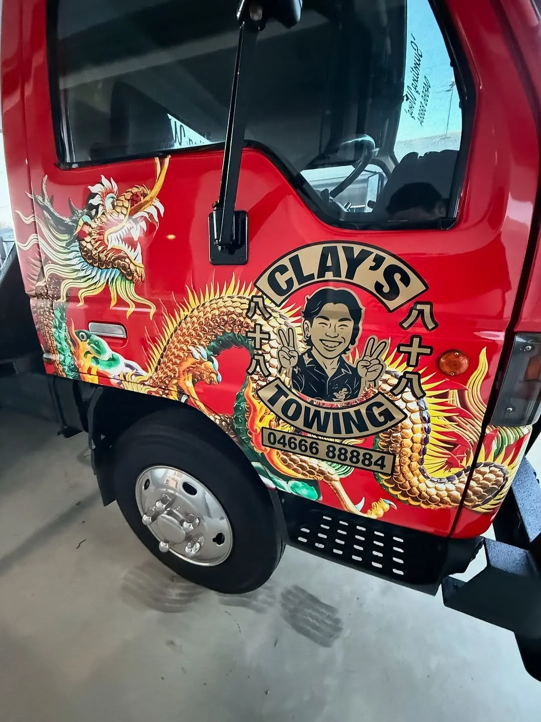 Decorated vehicle with traditional Asian dragon artwork, and a cartoon of a smiling man making peace signs, along with text 'Clay's Towing' and a phone number.