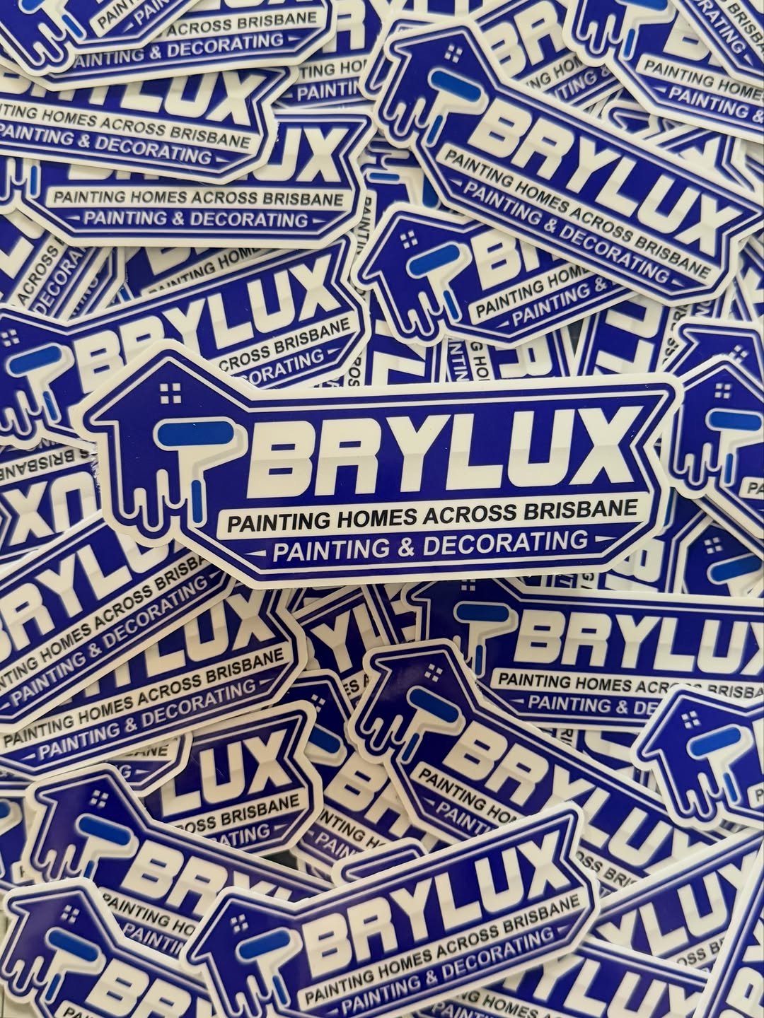 A collection of stickers for Brylux, a painting and decorating company, featuring a blue house with a paintbrush dripping paint, and text that reads 'Brylux, Painting Homes Across Brisbane, Painting & Decorating.'