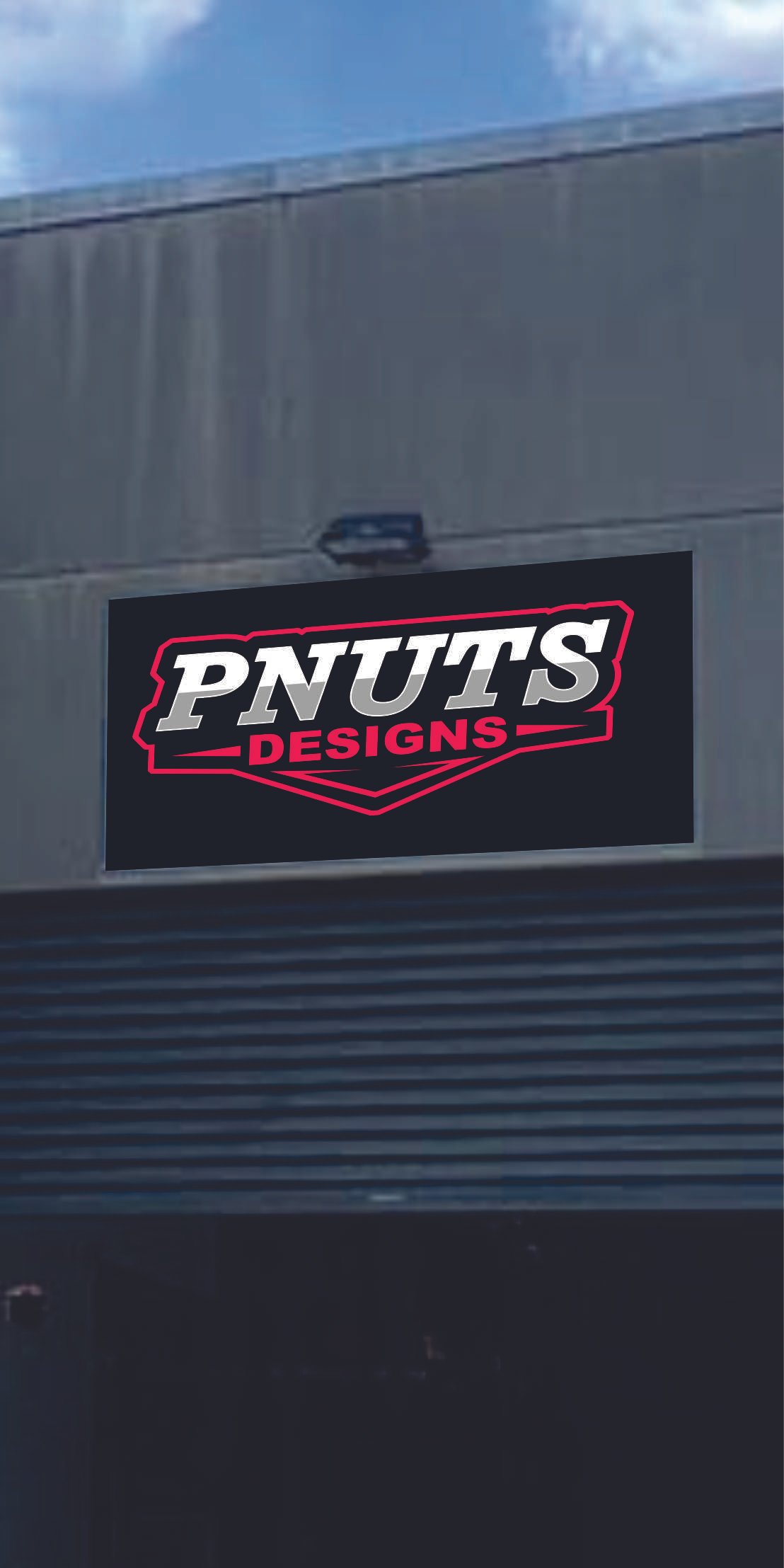 A black sign with red and white text that reads 'PNUTS DESIGNS' on a gray metallic wall.