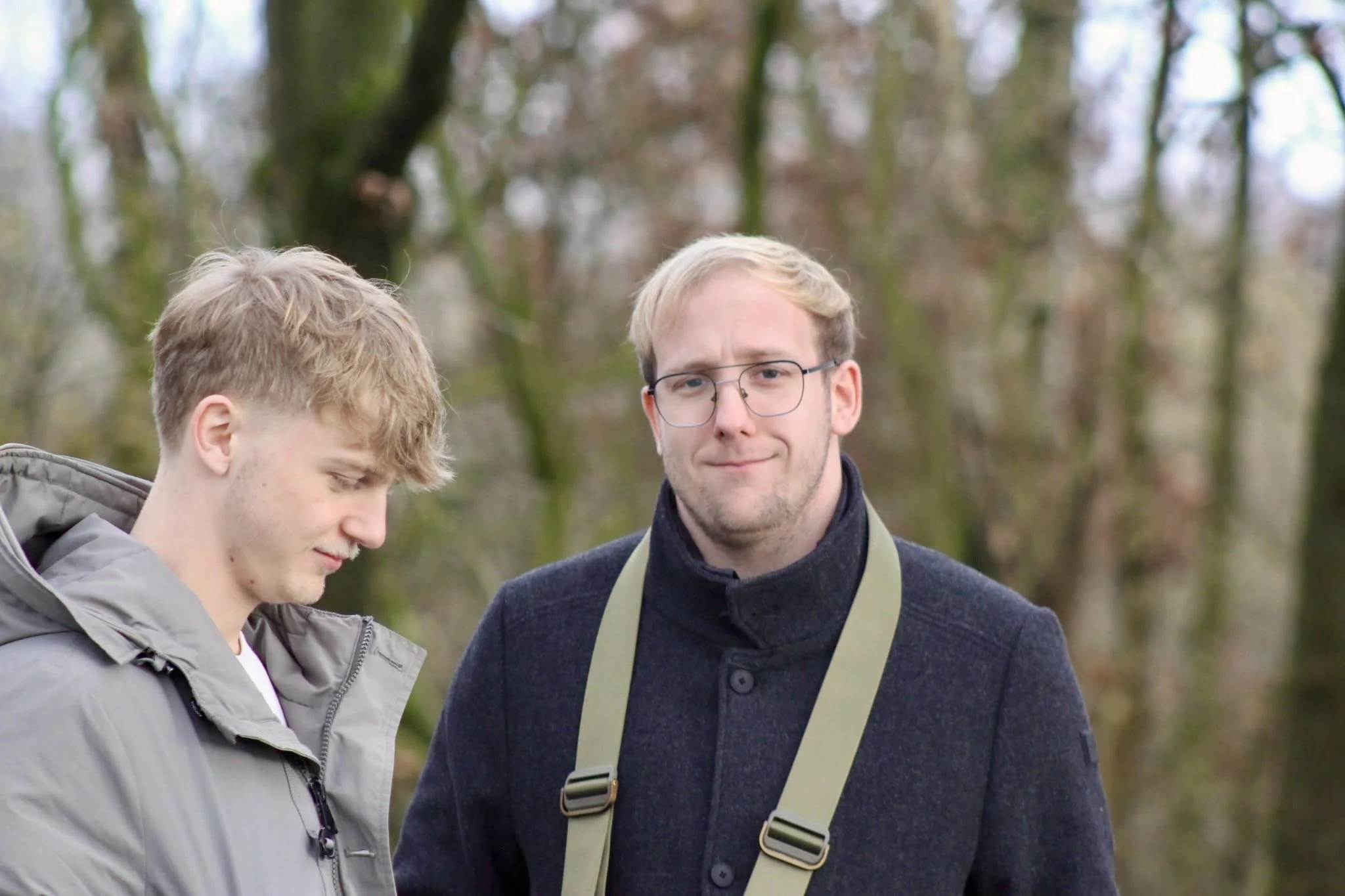 Twee jonge mannen wandelen samen in een bosachtige omgeving. Ze lijken vriendelijk en ontspannen.