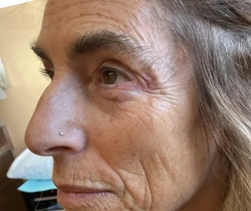 Close-up of an elderly woman’s face, showing wrinkles and a small nose piercing.