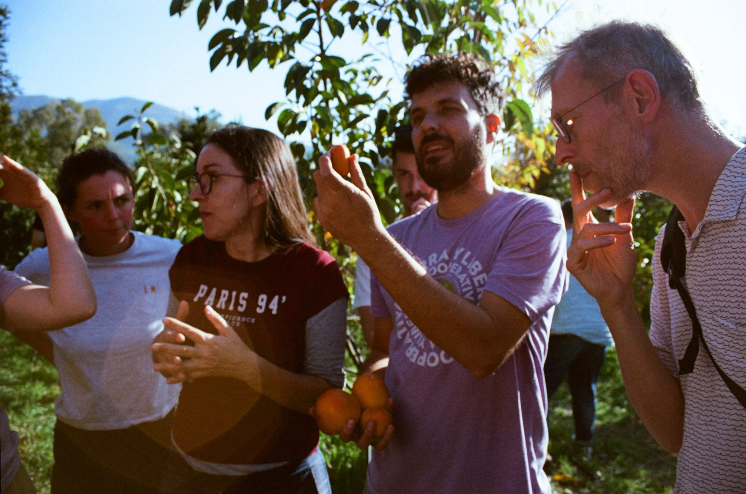 Groep mensen in een tuin, met enkele mensen die fruit vasthouden en met elkaar praten of lachen.