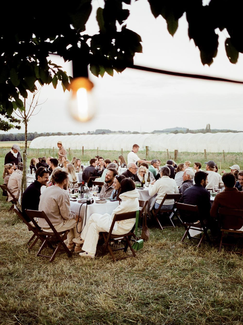 Mensen genieten van een buitenbijeenkomst of diner op grasdomeinen onder een boom tijdens de schemering.