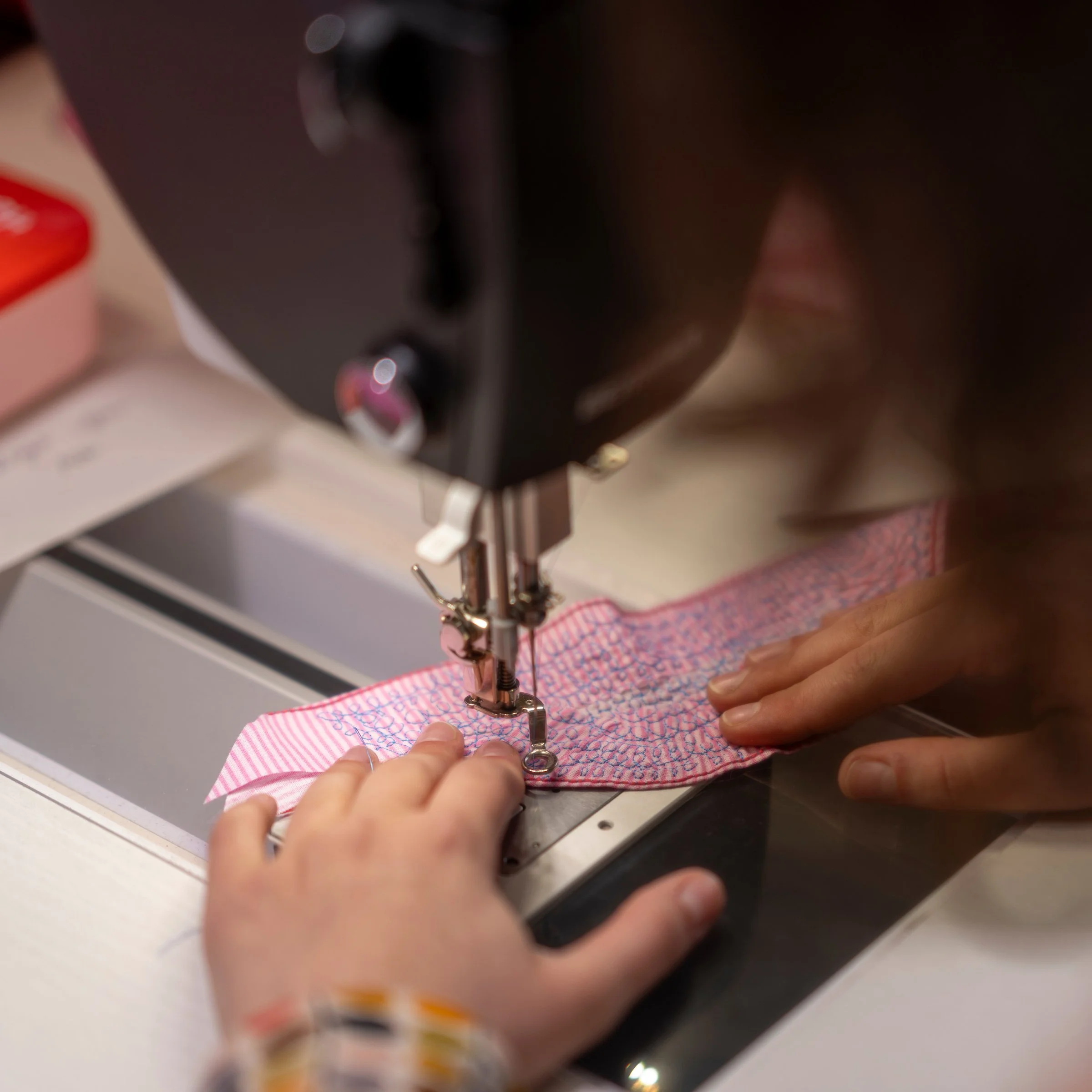 A person's hands sewing pink and white striped fabric by hand using a sewing machine.