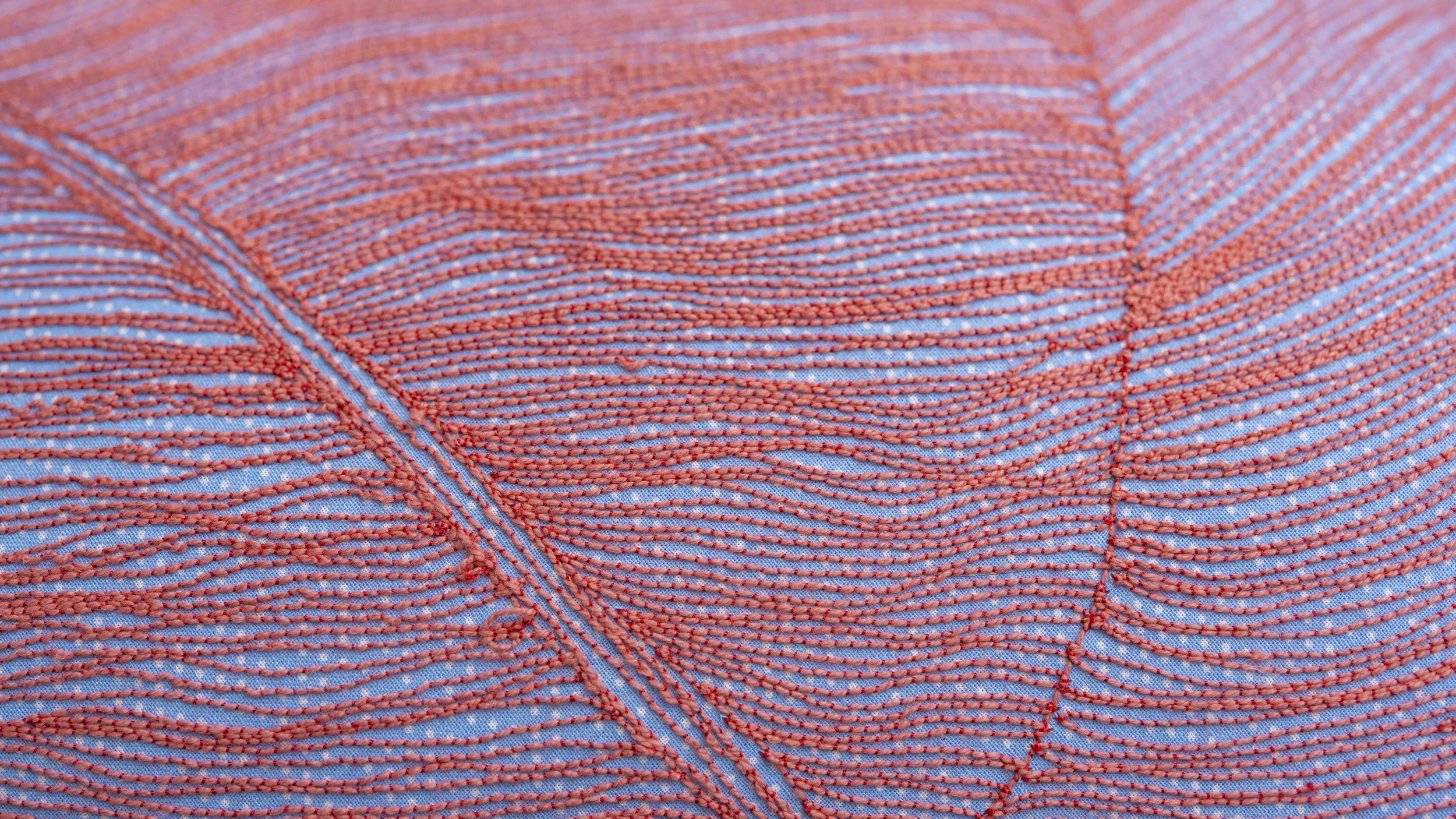 Close-up of blue fabric with orange embroidery stitched in parallel lines creating a textured pattern.