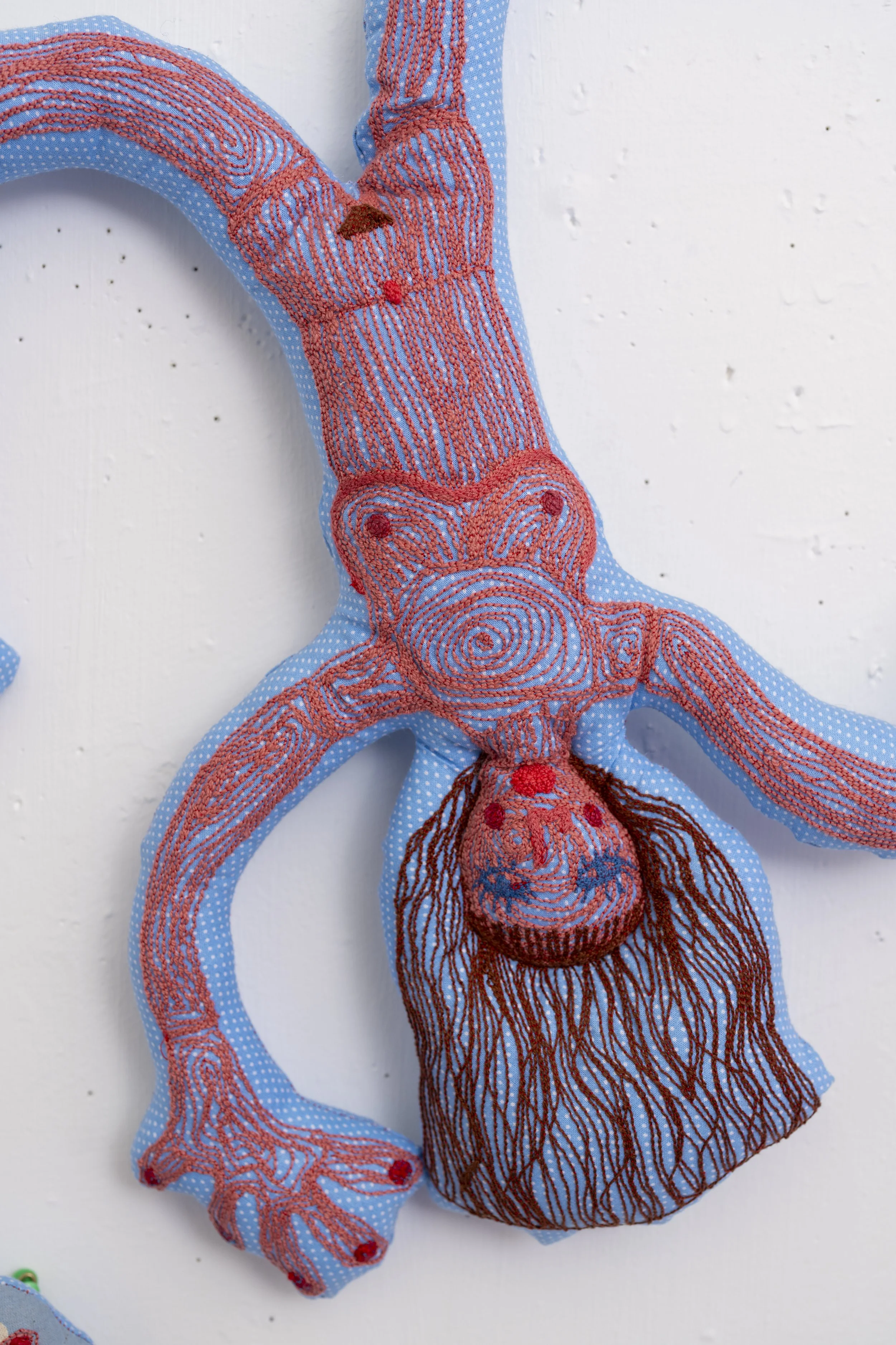 Textile art piece resembling an animal, made of blue fabric with red embroidery showing detailed anatomical features on a white surface.