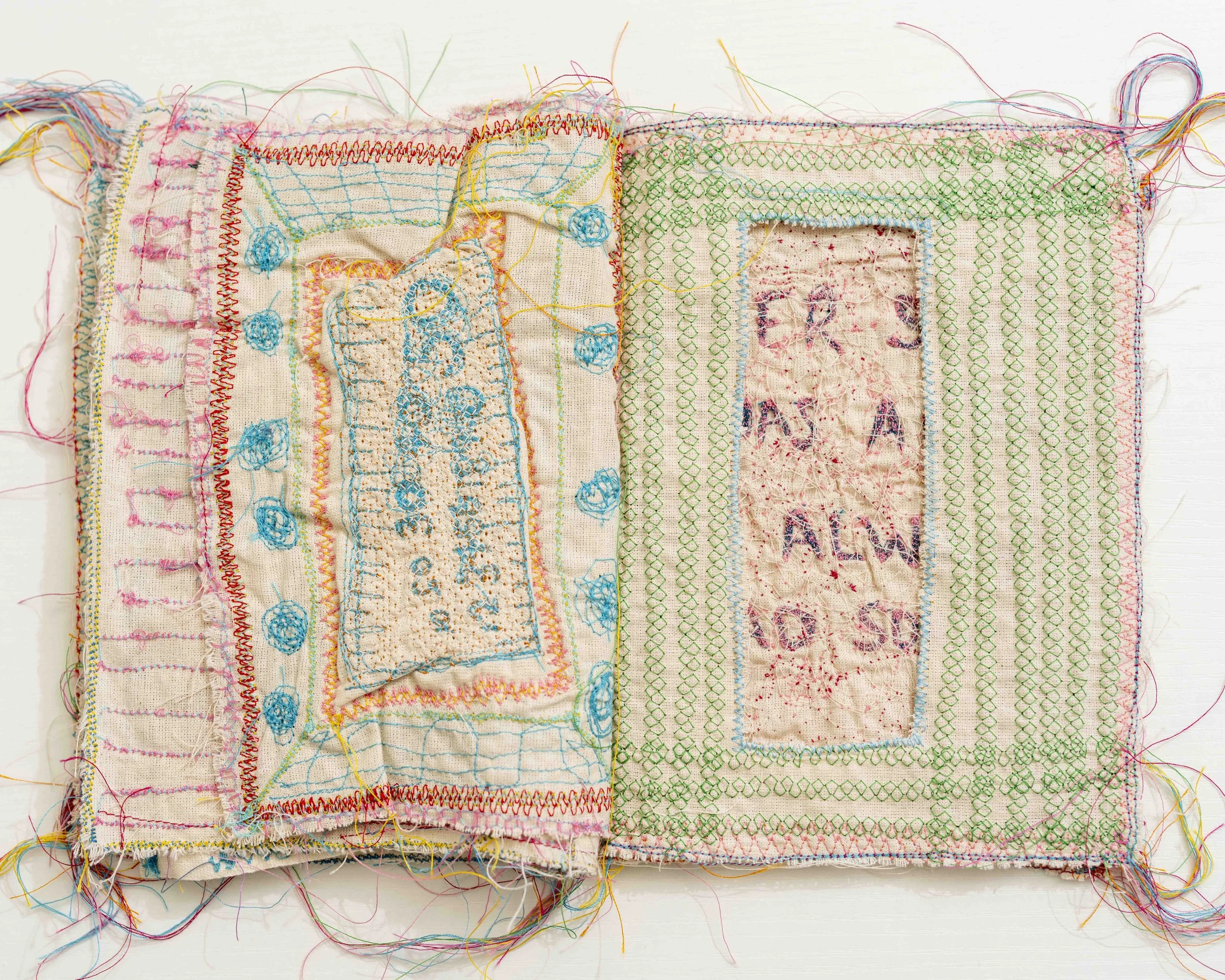 A piece of beige fabric with various colorful embroidery stitches and patterns, including grid, floral, and geometric designs, with loose threads at the edges.