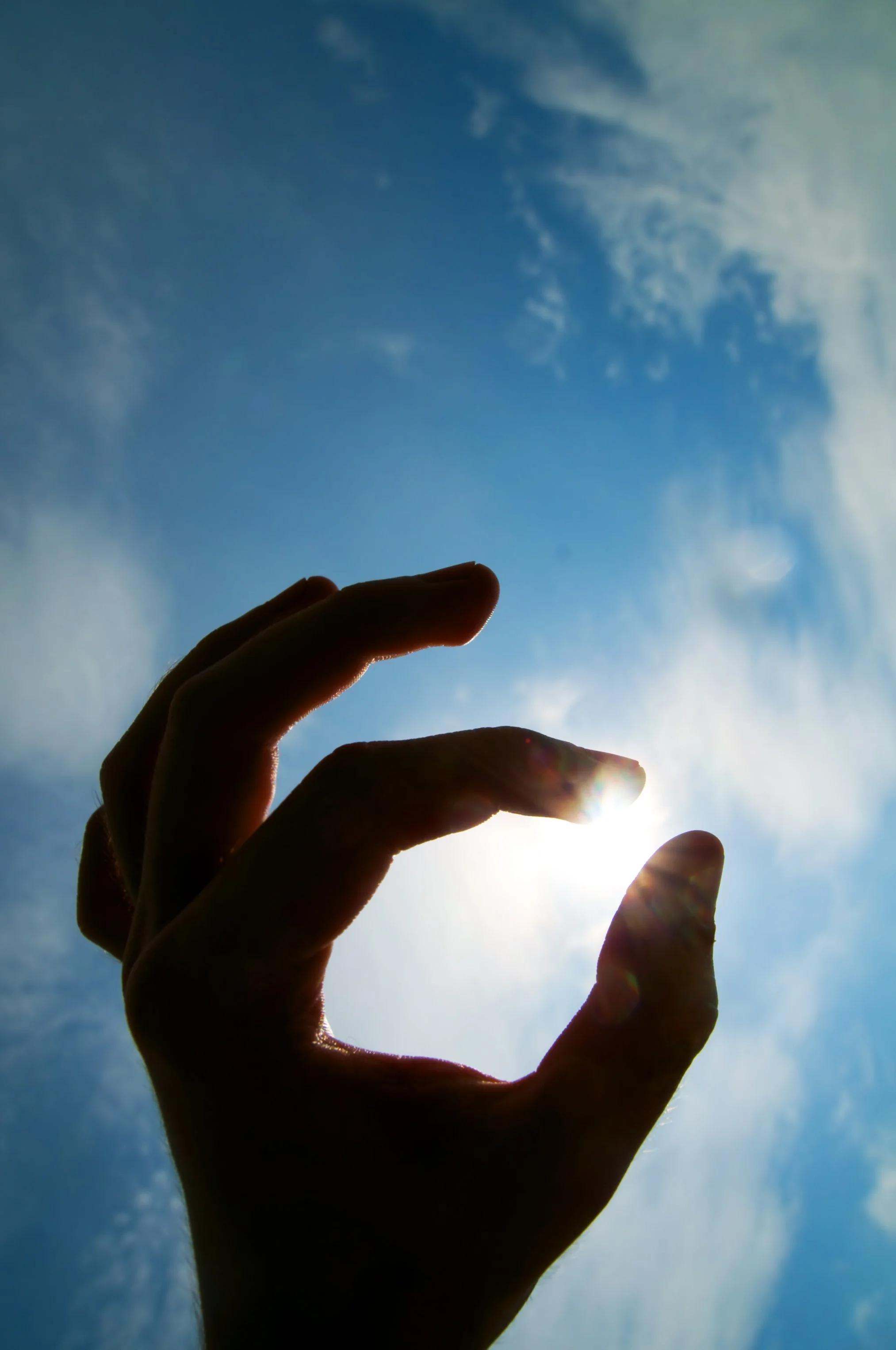 Una mano che si trova contro il cielo con nuvole e sole che brilla dietro le dita.