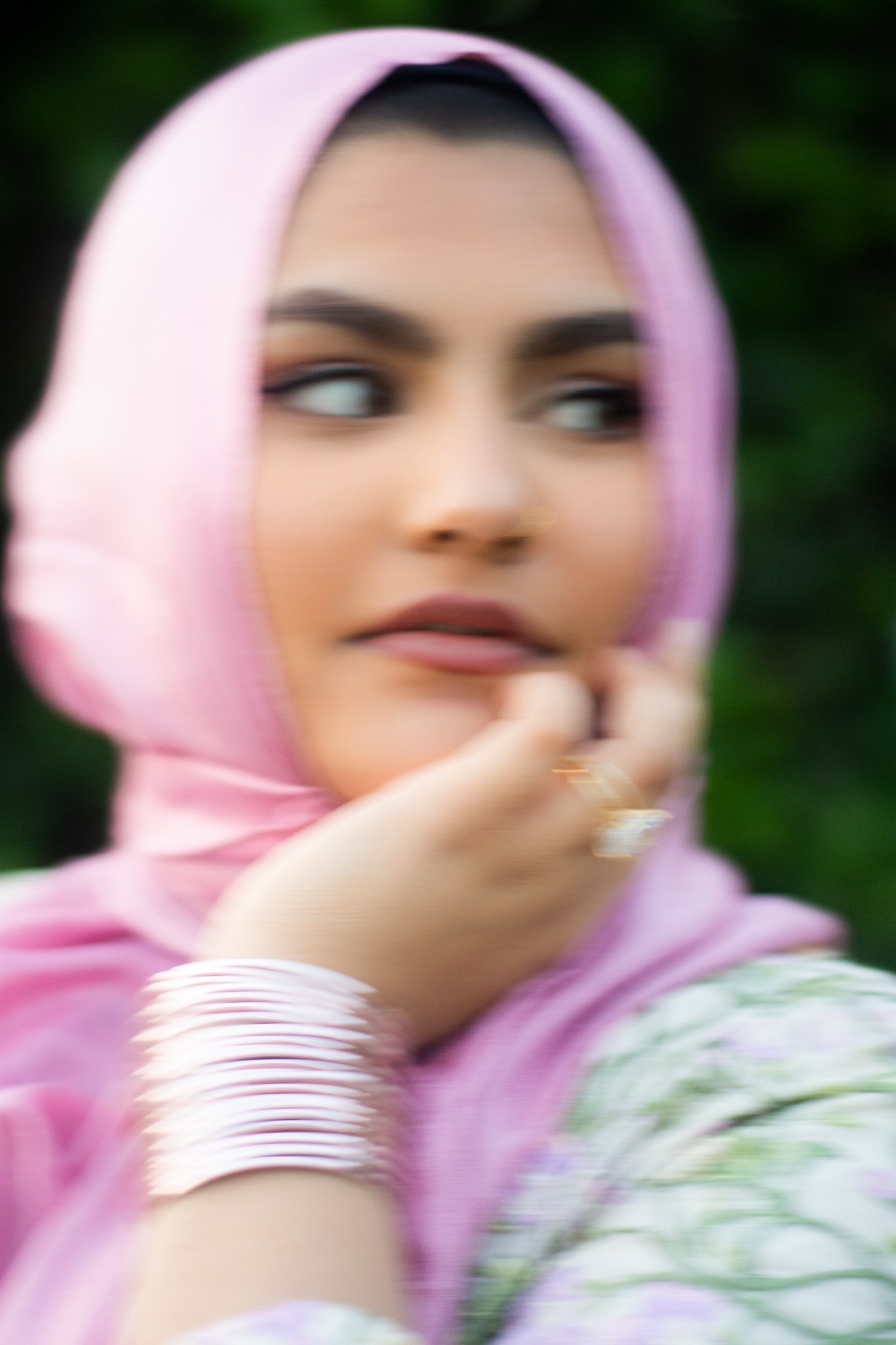 Close-up of a woman's face with defined eyebrows and eye makeup, wearing a pink headscarf, with green blurred background.