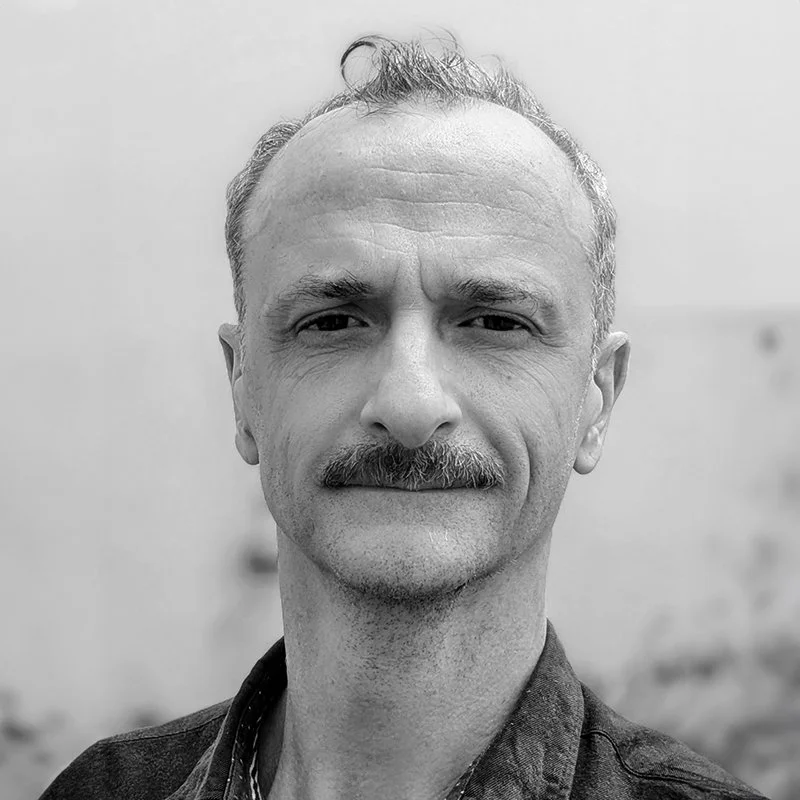 Black and white portrait of a man with a mustache, short hair, and a slight smile, wearing a collared shirt.