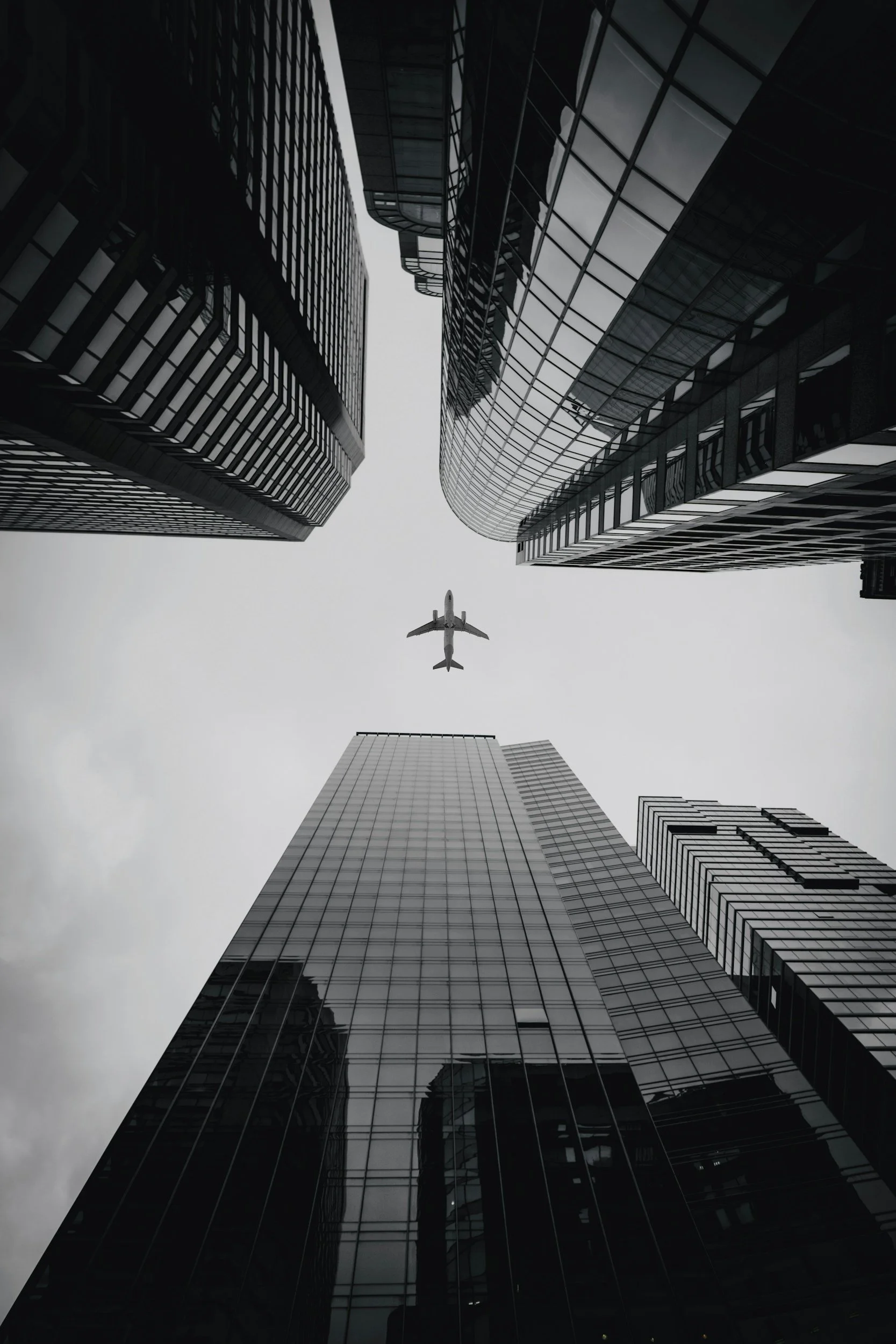 Looking up at tall modern glass skyscrapers in a city with an airplane flying between them.