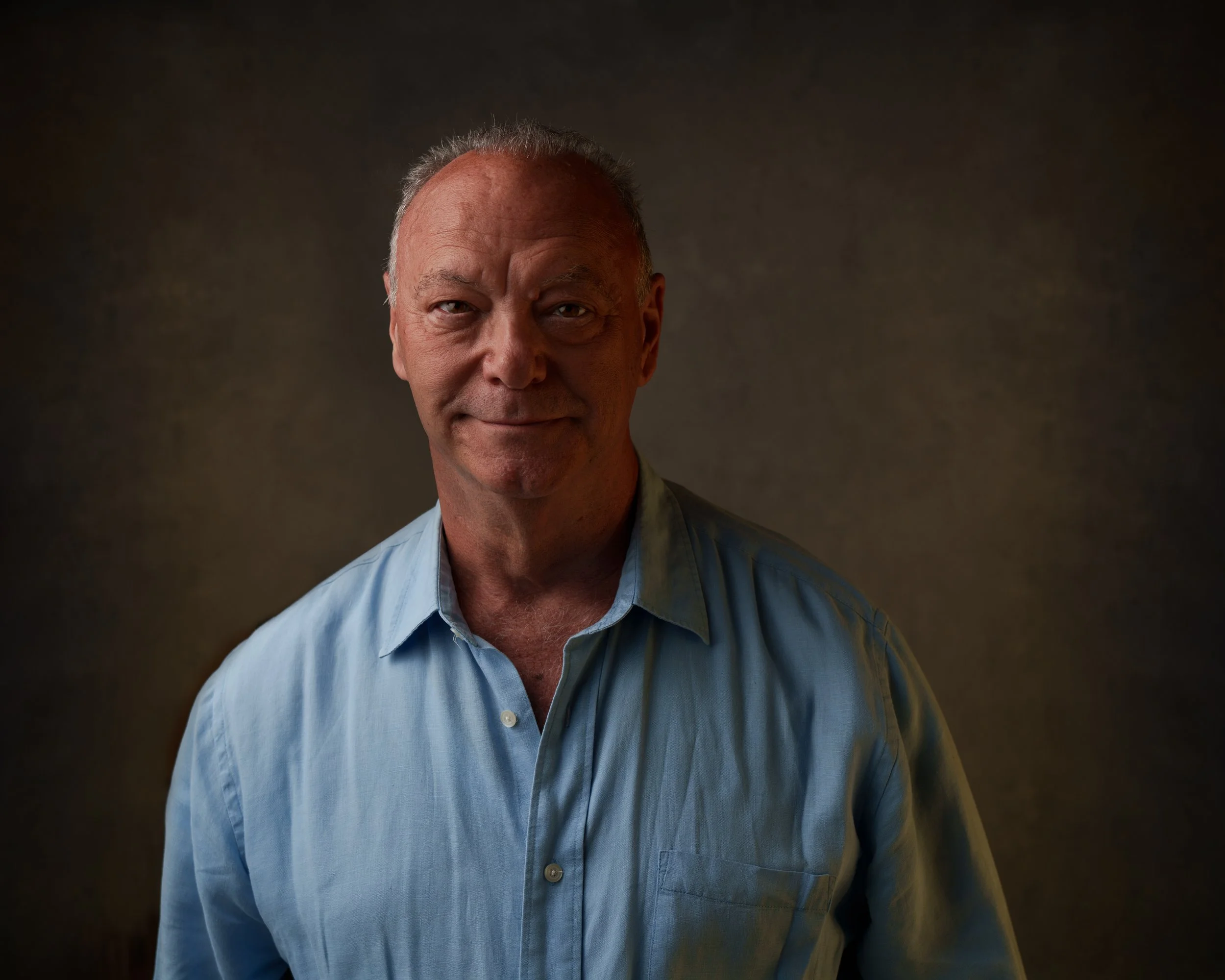 Close-up of a Michael Cannistraci wearing a light blue shirt, smiling slightly, with a dark, neutral background.