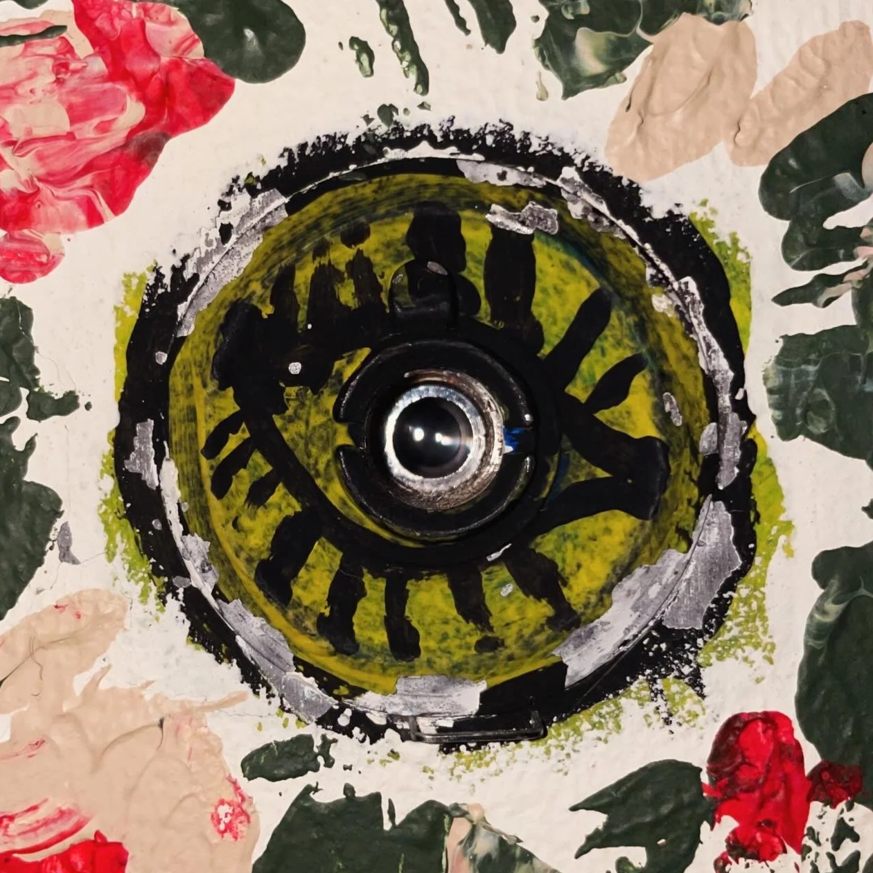 Close-up of a paint-splattered circular surface with black eye around a peephole, surrounded by floral patterns with red, pink, and green colors.