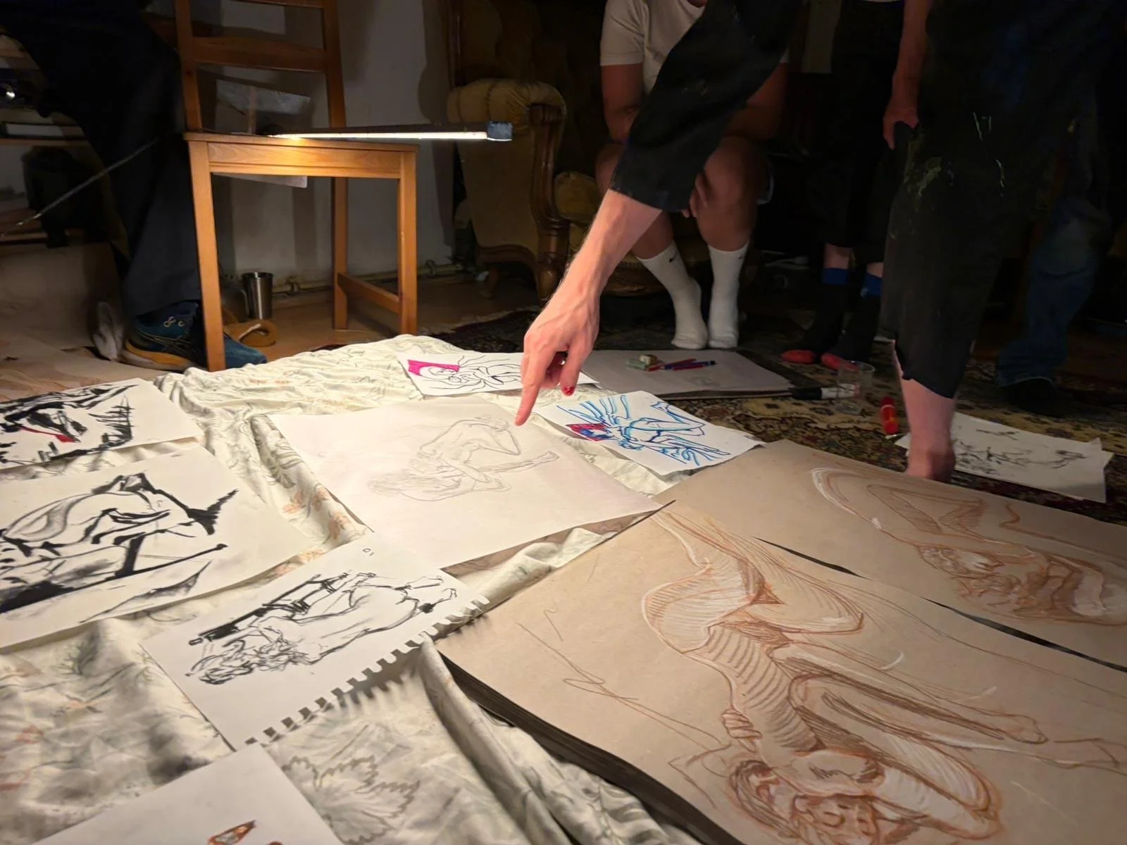 Group of people examining and displaying various sketches and drawings spread out on the floor of a room.