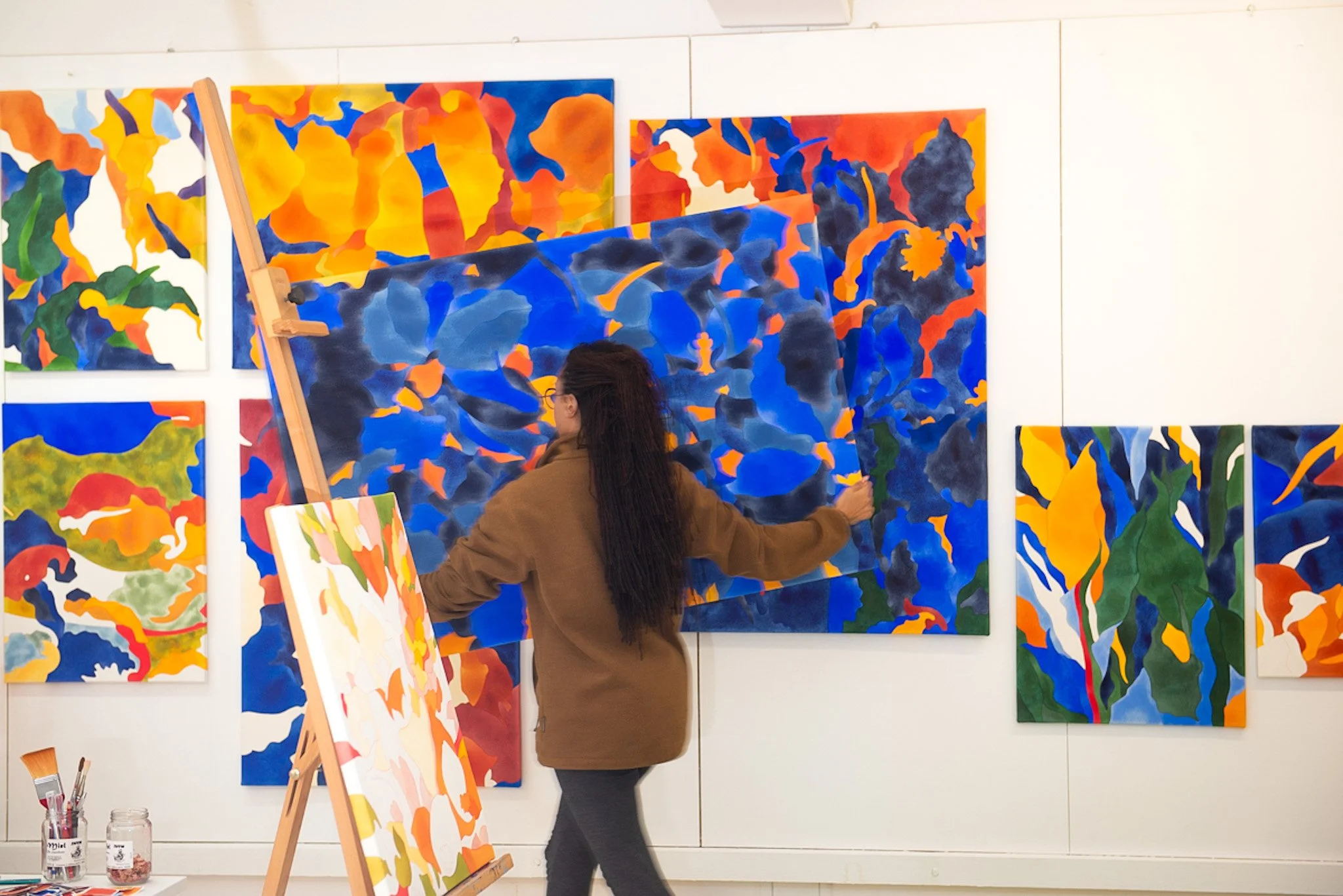 Une femme peint dans une galerie d'art avec plusieurs tableaux abstraits colorés en arrière-plan.