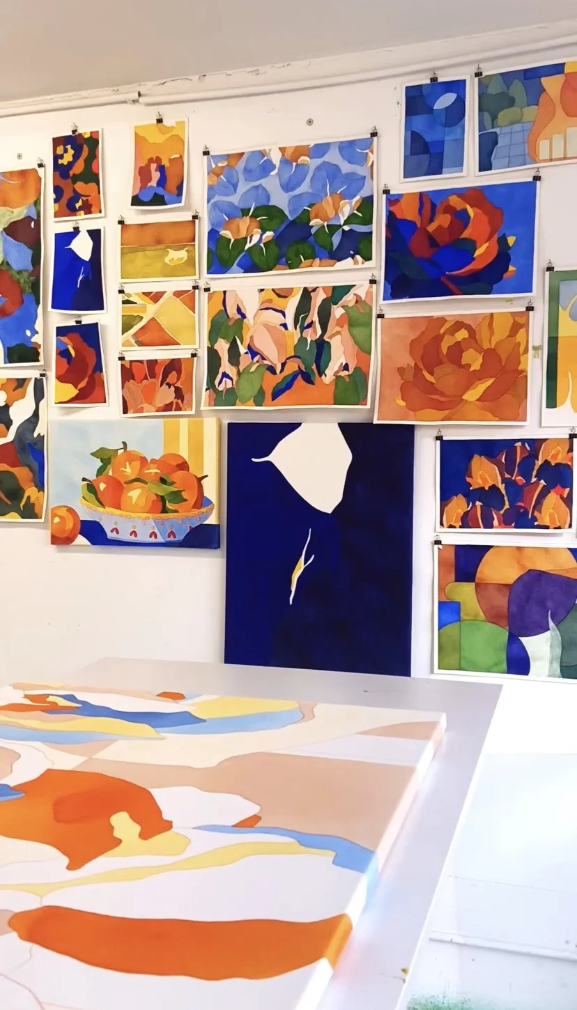 Une exposition d'œuvres d'art modernes et abstraites, principalement composées de peintures avec des couleurs vives et chaudes, représentant des fleurs, des fruits et des formes géométriques sur un mur blanc.