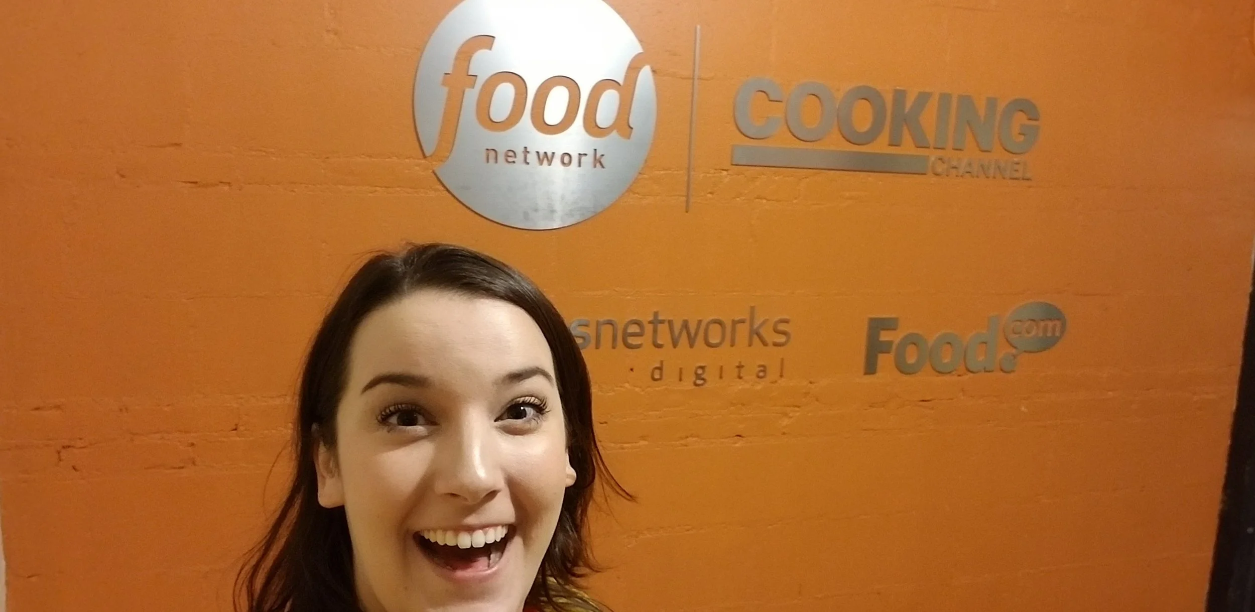 Close-up of a young woman smiling in front of an orange wall with logos for 'food network' and 'cooking channel'.