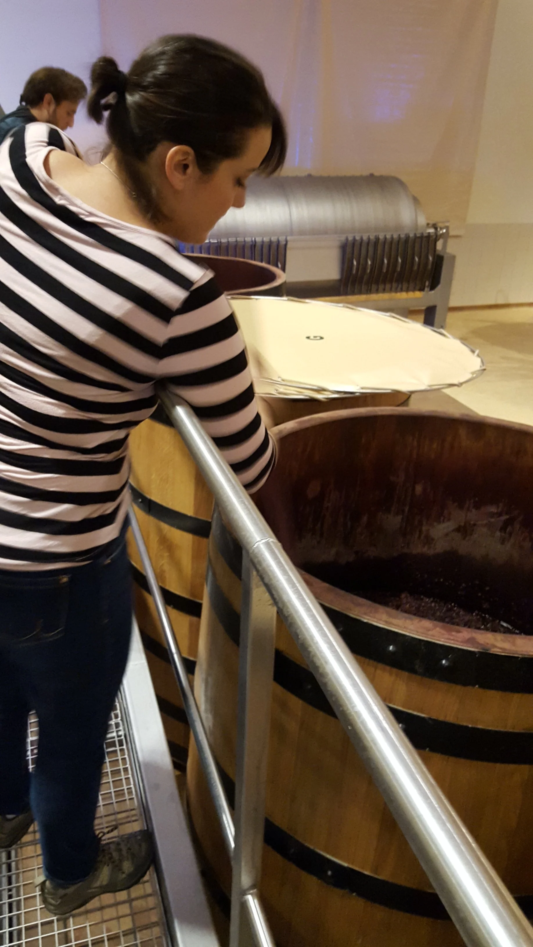 A woman in a striped shirt stirring a large barrel of dark liquid.
