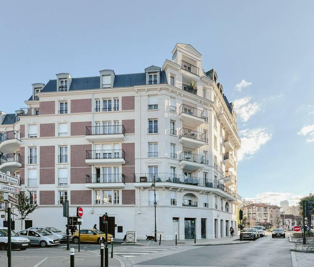 Un immeuble résidentiel coloré avec plusieurs balcons et fenêtres, situé à un croisement avec des voitures stationnées et une signalisation routière.
