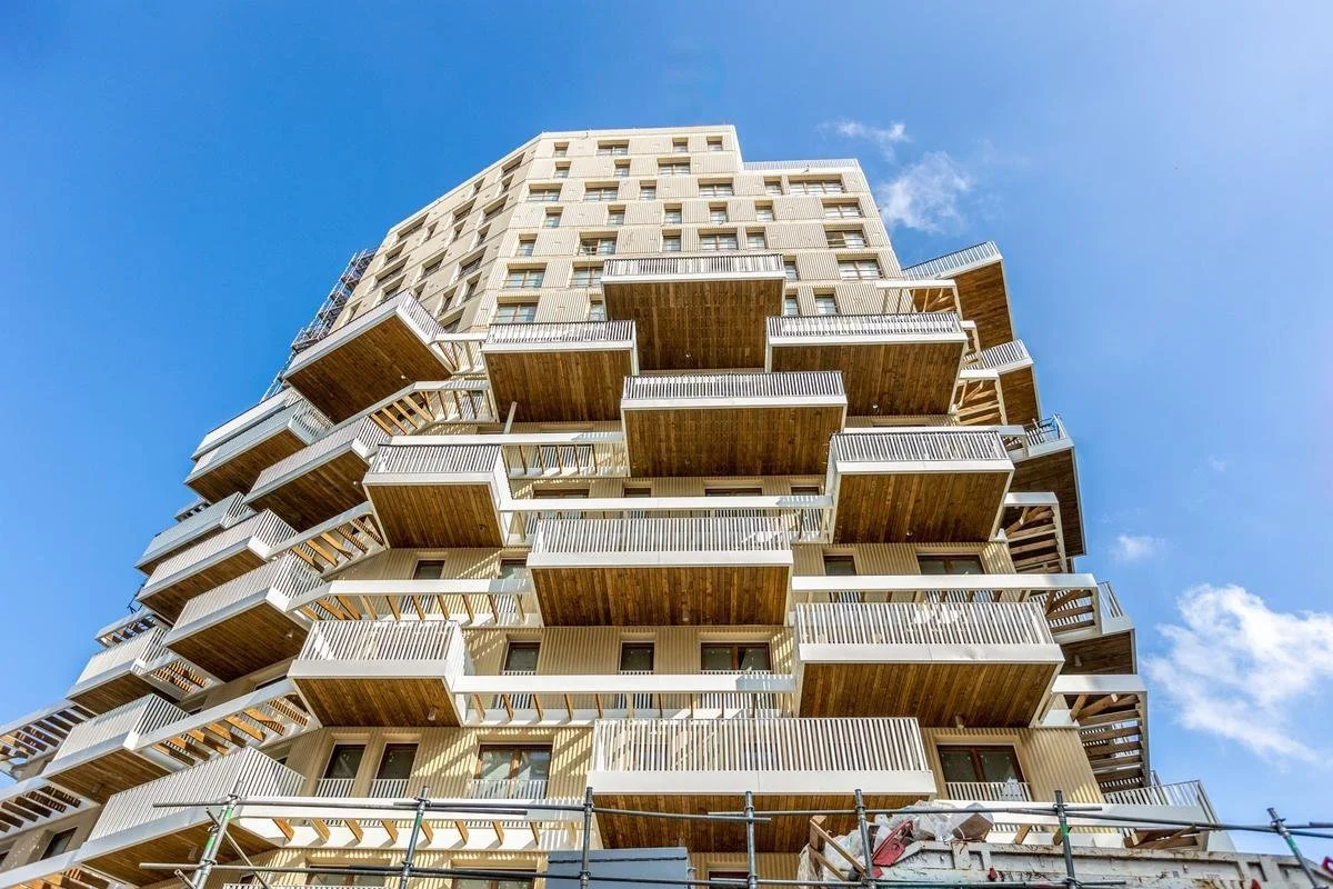 Immeuble moderne avec plusieurs balcons en bois sous un ciel bleu.