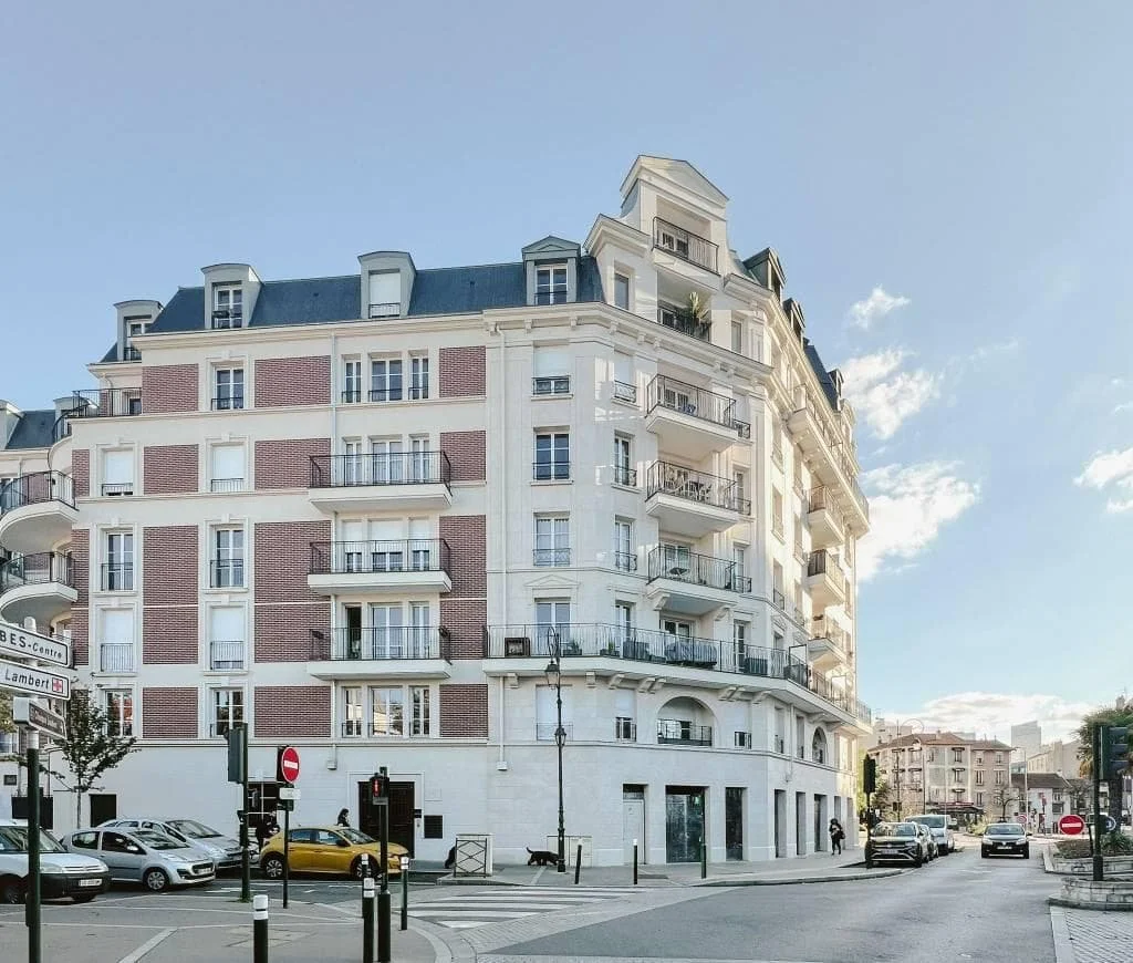 Un immeuble résidentiel coloré avec plusieurs balcons et fenêtres, situé à un croisement avec des voitures stationnées et une signalisation routière.