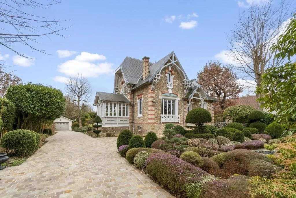 Une maison de style victorien avec un jardin bien entretenu, des buissons taillés et un chemin pavé