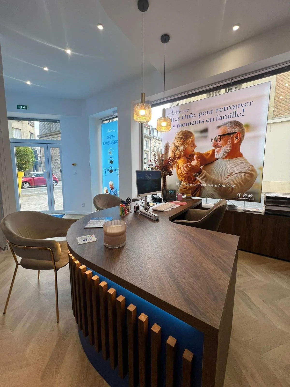Intérieur d'un bureau avec une table, des chaises, un ordinateur, et une grande affiche de décoration représentant un homme et une fille qui sourient.