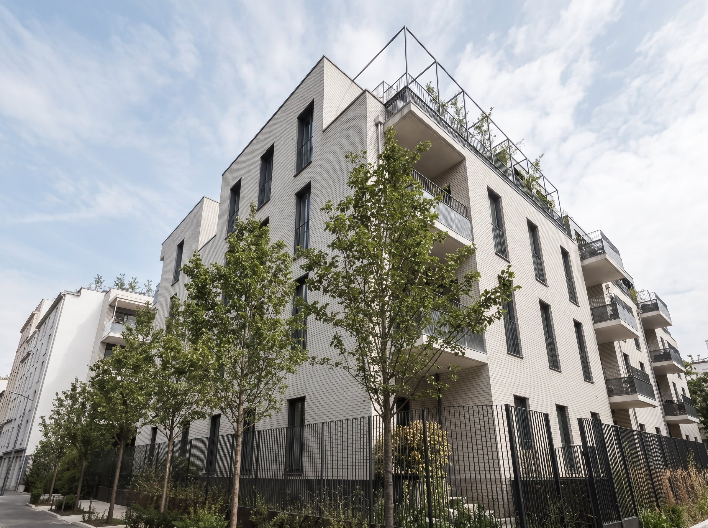 Immeuble résidentiel moderne avec plusieurs étages, entouré d'arbres et de balcons, sous un ciel partiellement nuageux.
