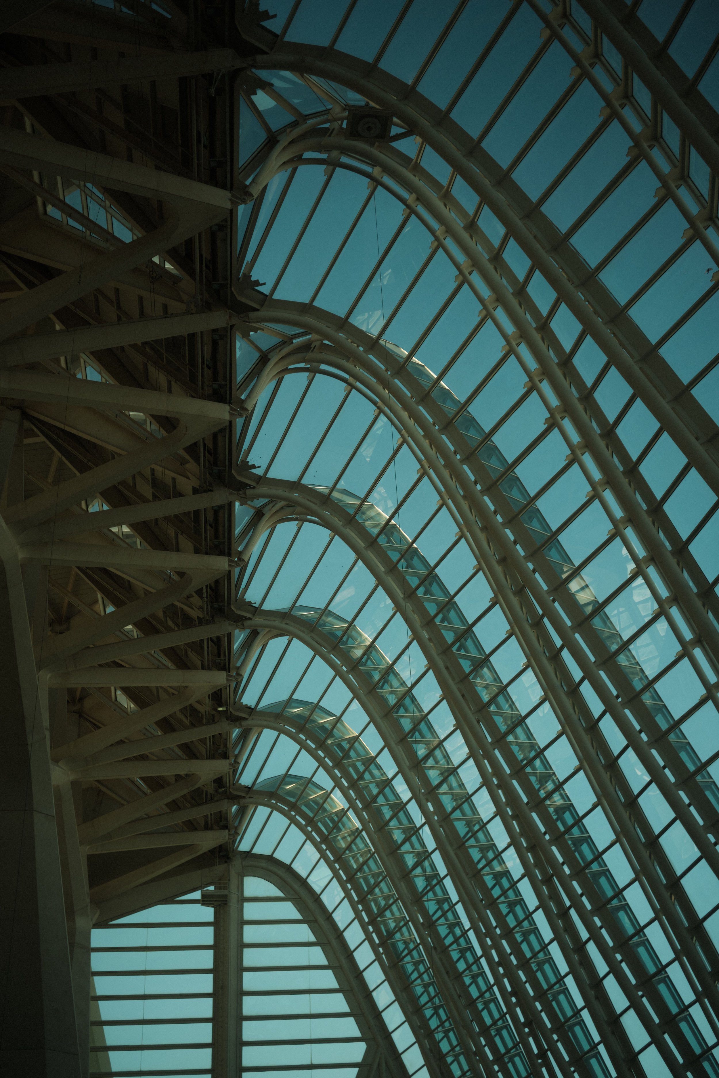 Intérieur d'une structure architecturale moderniste avec de grandes arches en acier et des fenêtres en verre laissant passer la lumière naturelle.