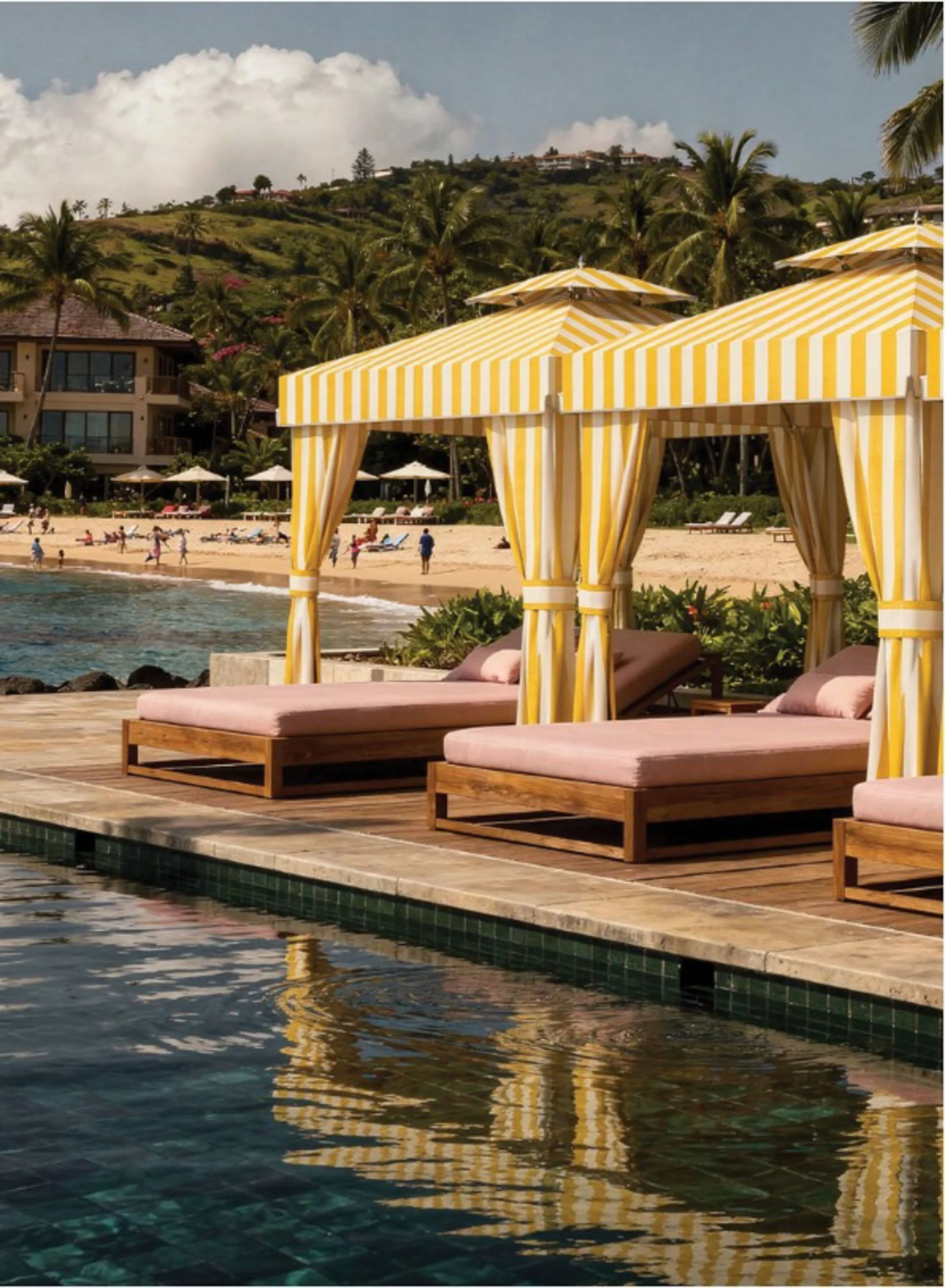 Beachside lounge chairs under yellow and white striped cabanas next to a swimming pool, with a sandy beach and people in the background, hillside with lush vegetation and buildings, tropical palm trees, partly cloudy sky.