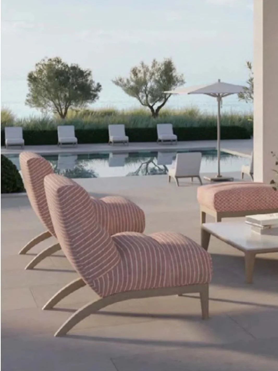 Outdoor patio with pink and white striped lounge chairs, a white coffee table, and a swimming pool with additional white lounge chairs and an umbrella, overlooking a landscape with trees and grass.