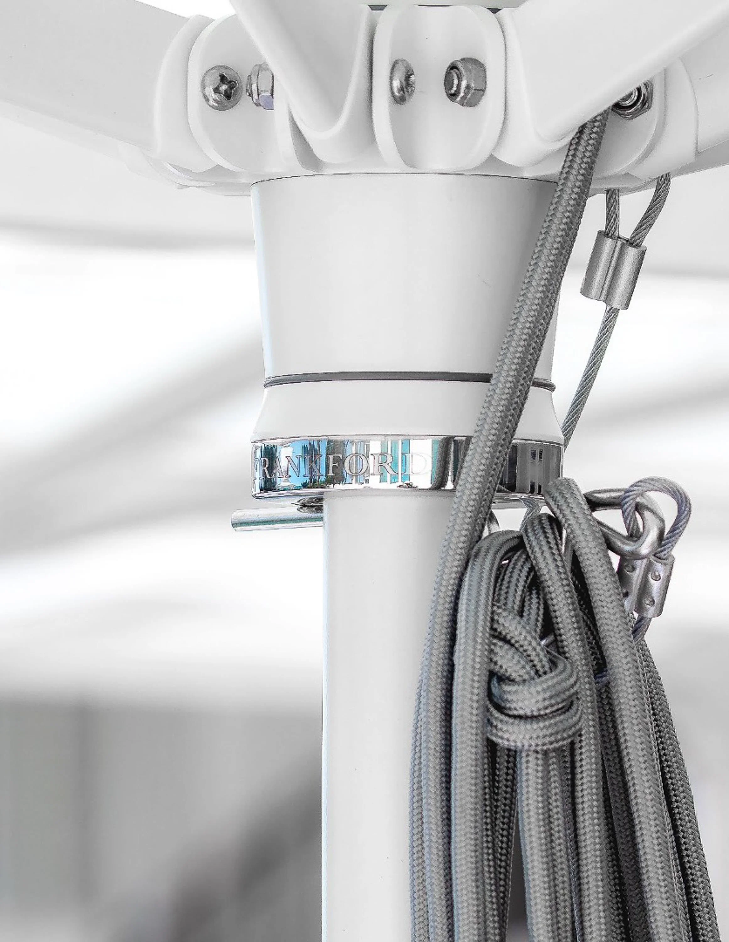 Close-up of an electric cord organizer with gray fabric cords secured by a metal clamp, attached to a white wall or ceiling mount with screws, under bright lighting.