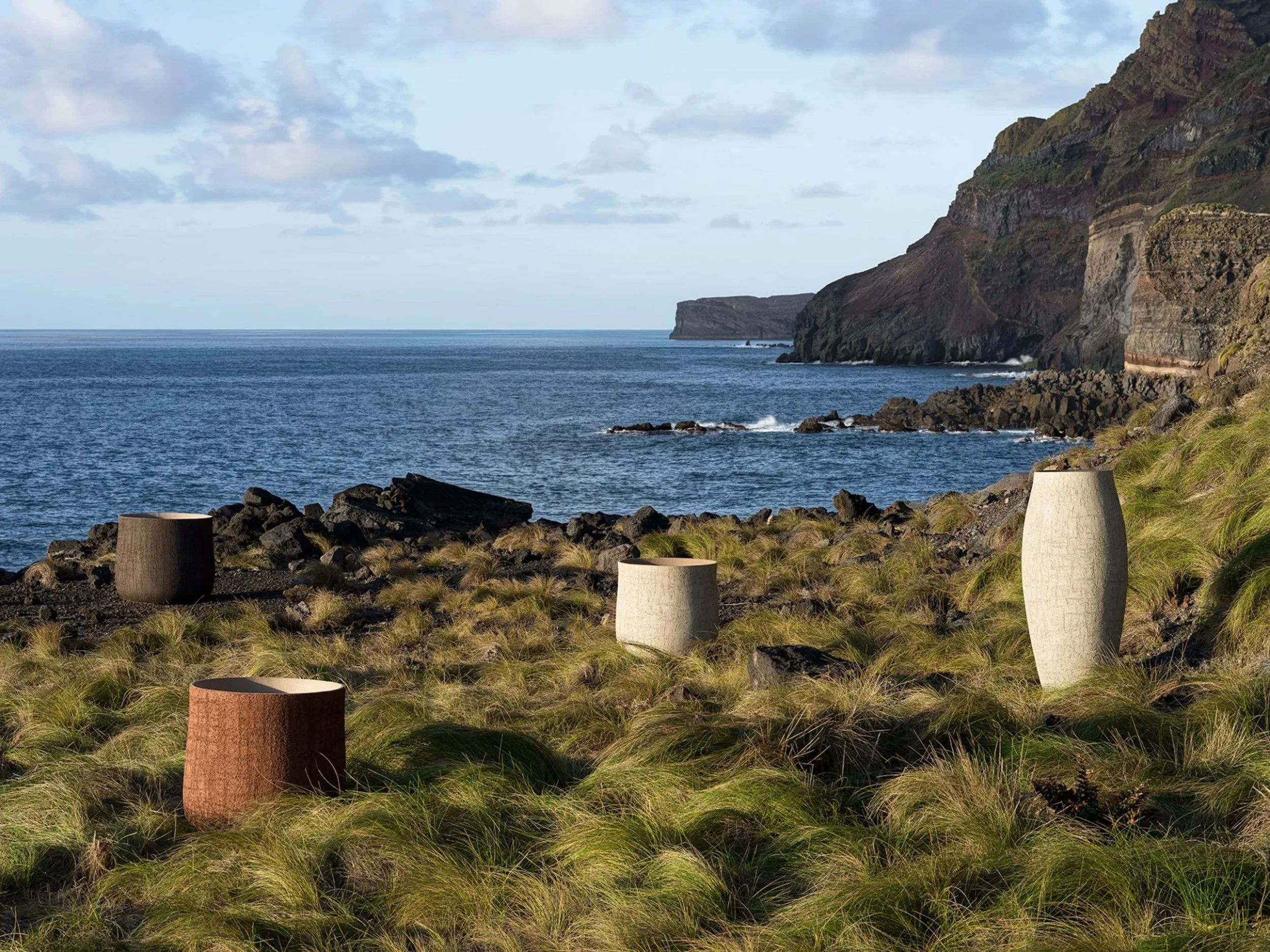 Cliffs overlooking the ocean with grassy foreground and decorative large stone and wood cylindrical objects.