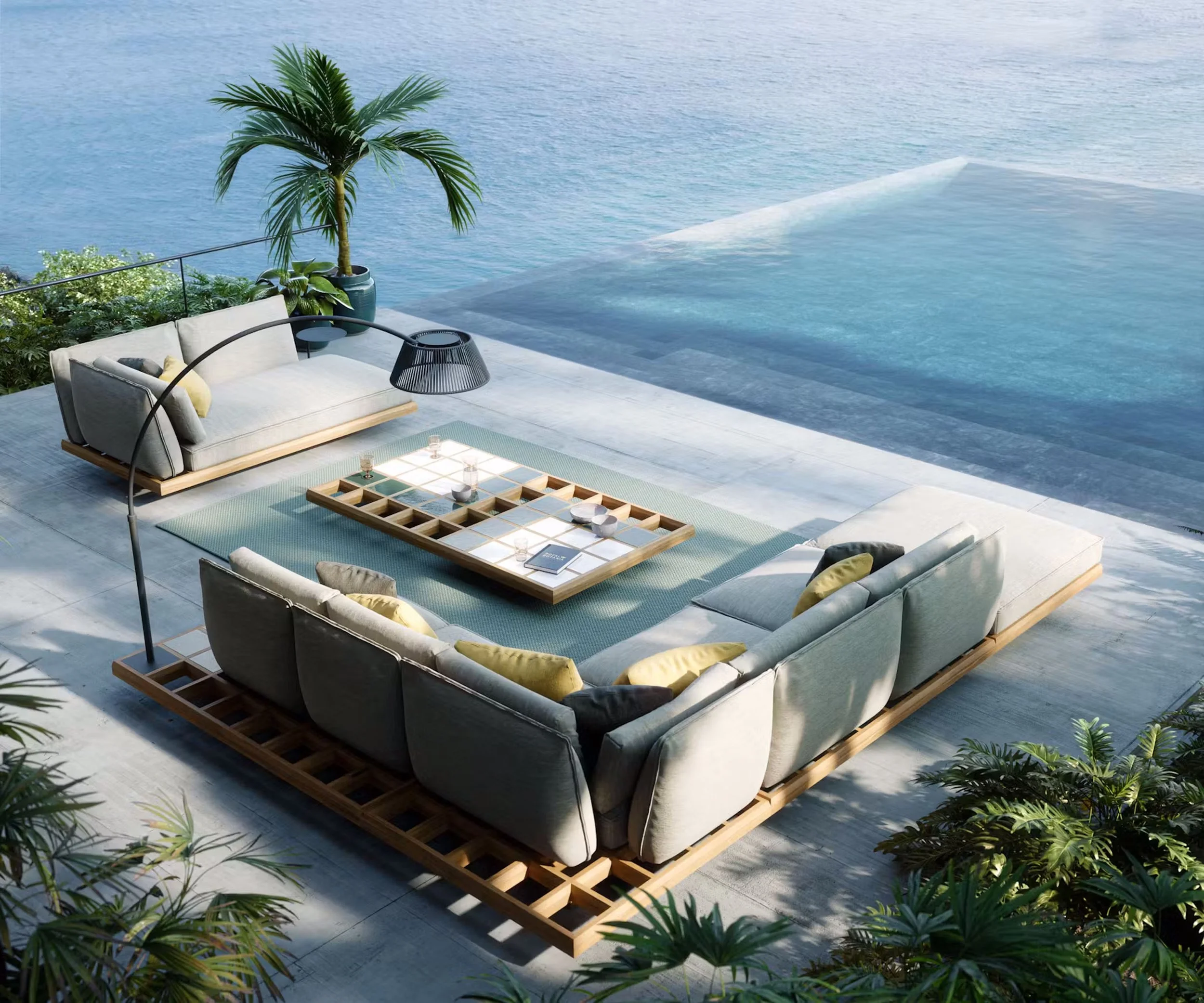 Outdoor seating area with a white cushioned sofa, black wire-frame lamp, and low wooden tables on a patio with steps leading into a swimming pool, overlooking a large body of water.