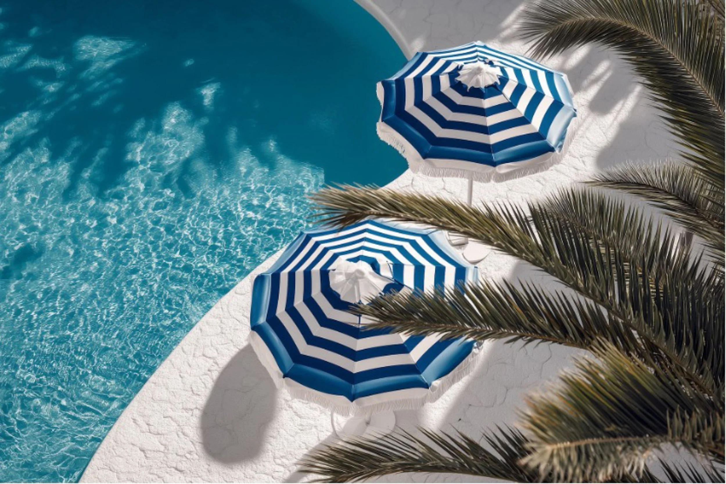 View of a swimming pool with blue water, white deck, two blue and white striped umbrellas, and palm tree shadows.