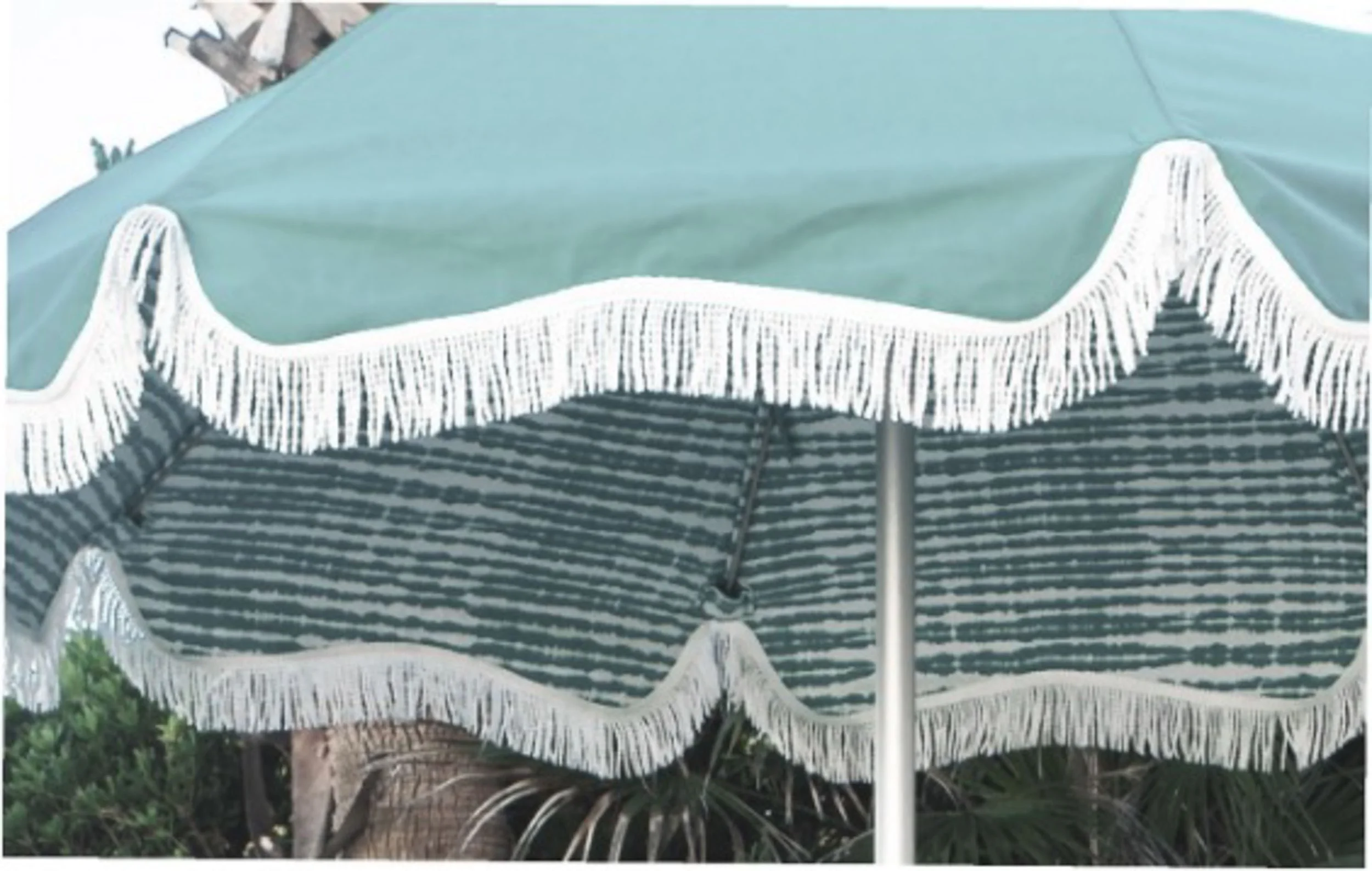 Close-up of a patio umbrella with a black and white striped pattern and white fringe trim, set outdoors with greenery in the background.