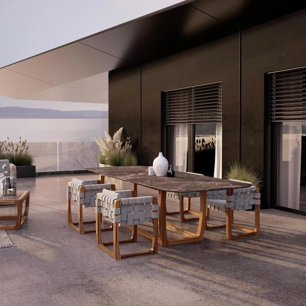 Modern outdoor patio with a wooden dining table, woven chairs, decorative vases, and plants, overlooking a scenic water view.