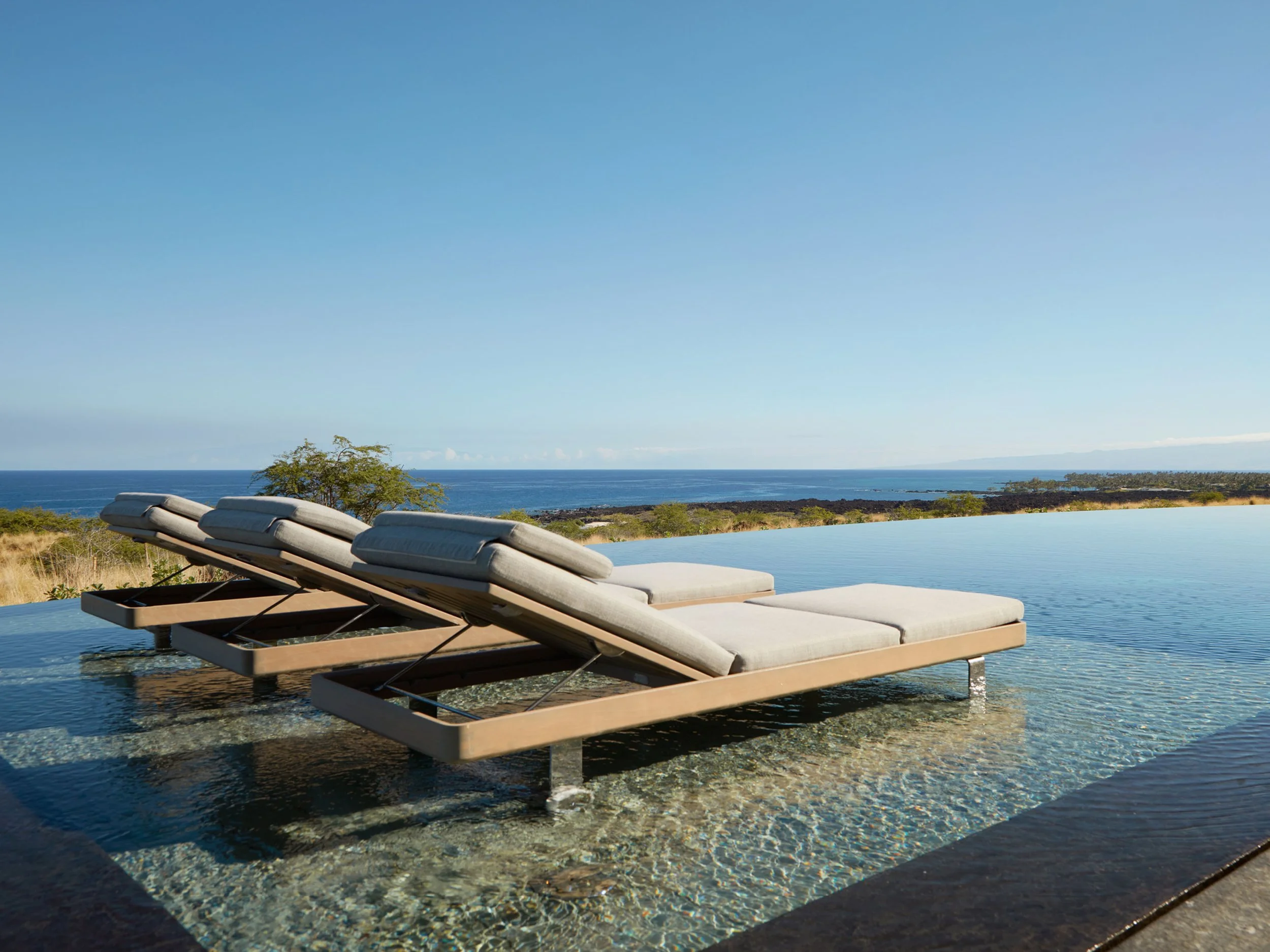A scenic view of a swimming pool with lounge chairs facing the ocean and sky in the background.