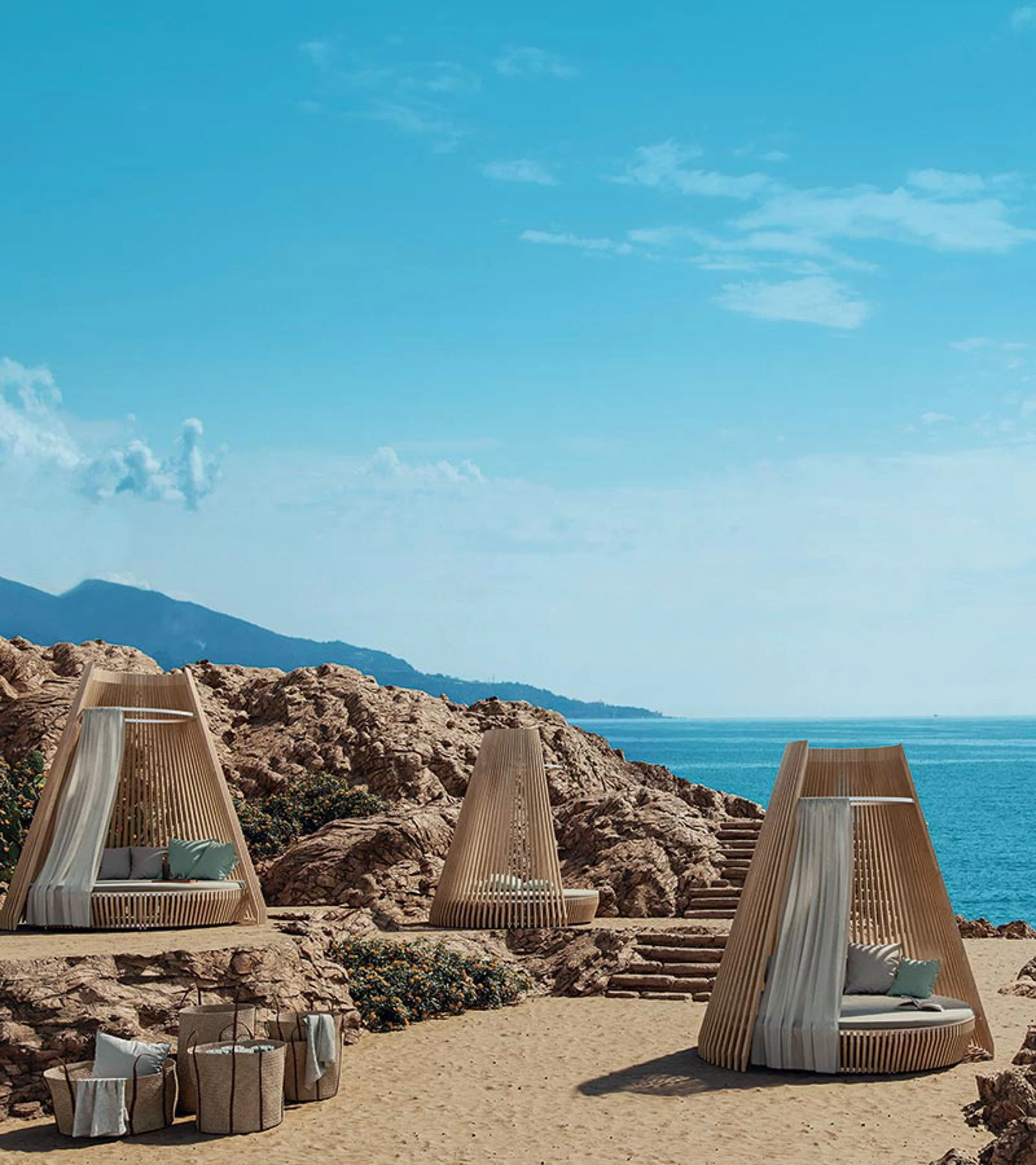 Beach scene with modern wooden lounge chairs on sandy shore, rocky formations, and ocean in the background with a clear blue sky.