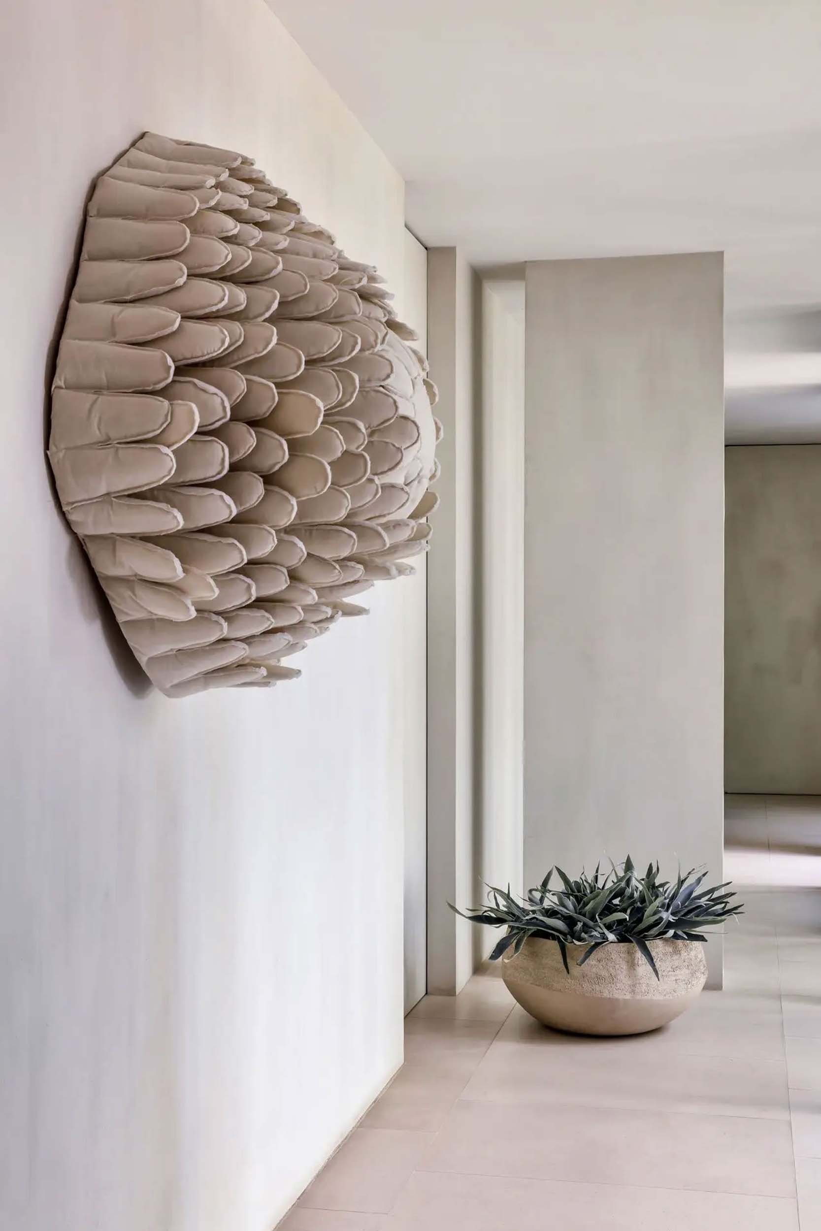 Modern interior with a large decorative beige flower sculpture on the wall and a potted plant with spiky leaves in the corner.