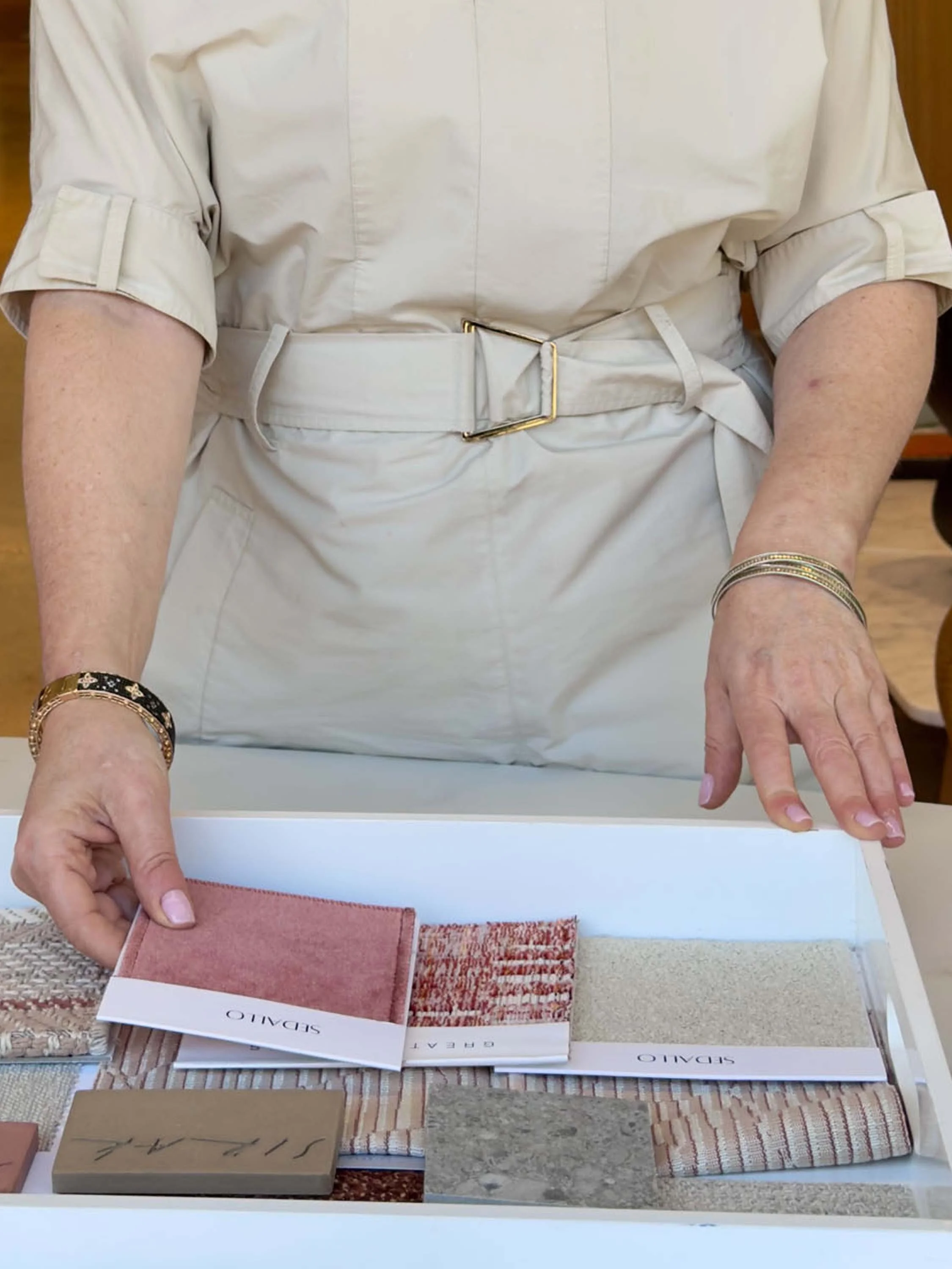 Close-up of a person showing fabric sample book with different textures and colors, including brick, sand, and plush swatches, on a table.