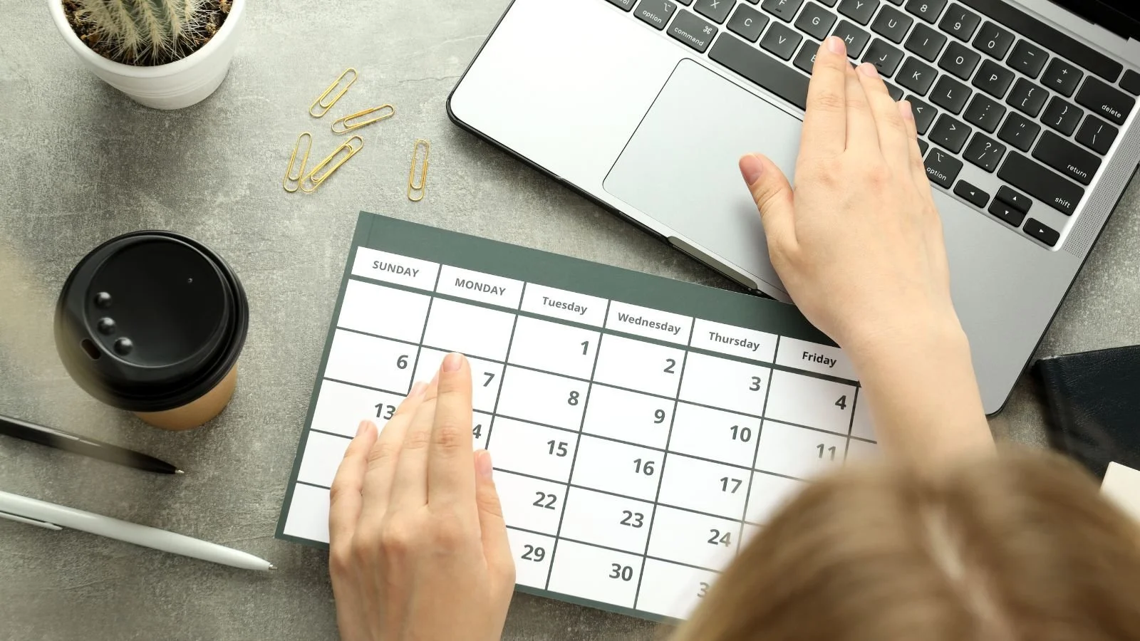 A traveler working on their laptop while looking at the calendar to plan ahead for a vacation