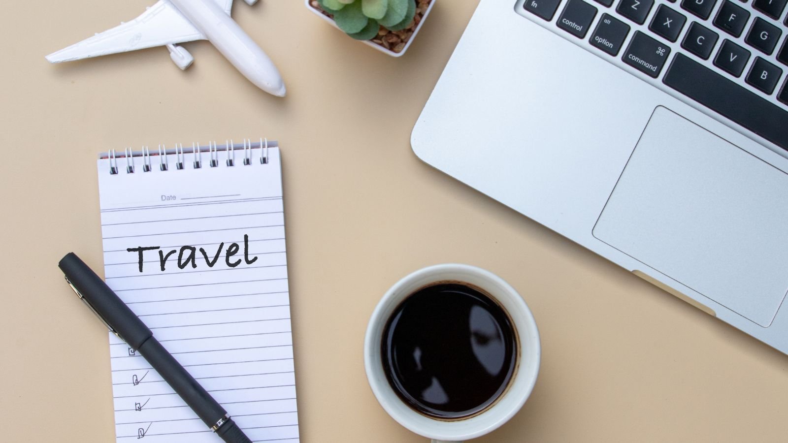 Laptop, notebook, coffee, and travel planning supplies on a desk while planning a vacation.